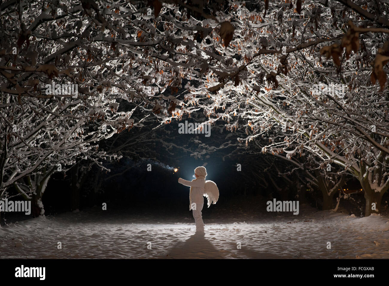 Ailes d'ange enfant vêtu blanc tenant une lumière dans nuit d'hiver Banque D'Images