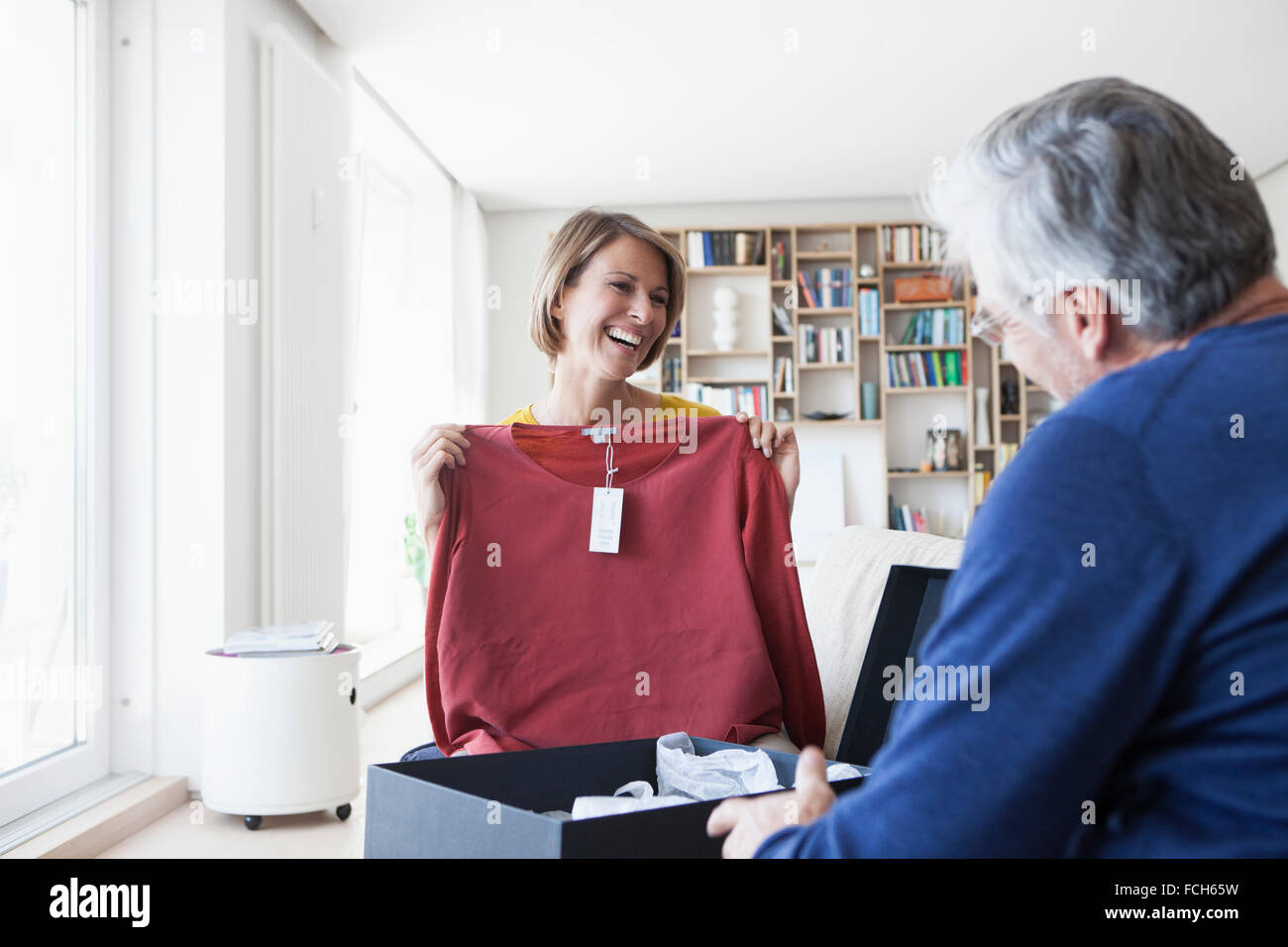 Smiling woman showing mari son nouveau pull dans le salon Banque D'Images