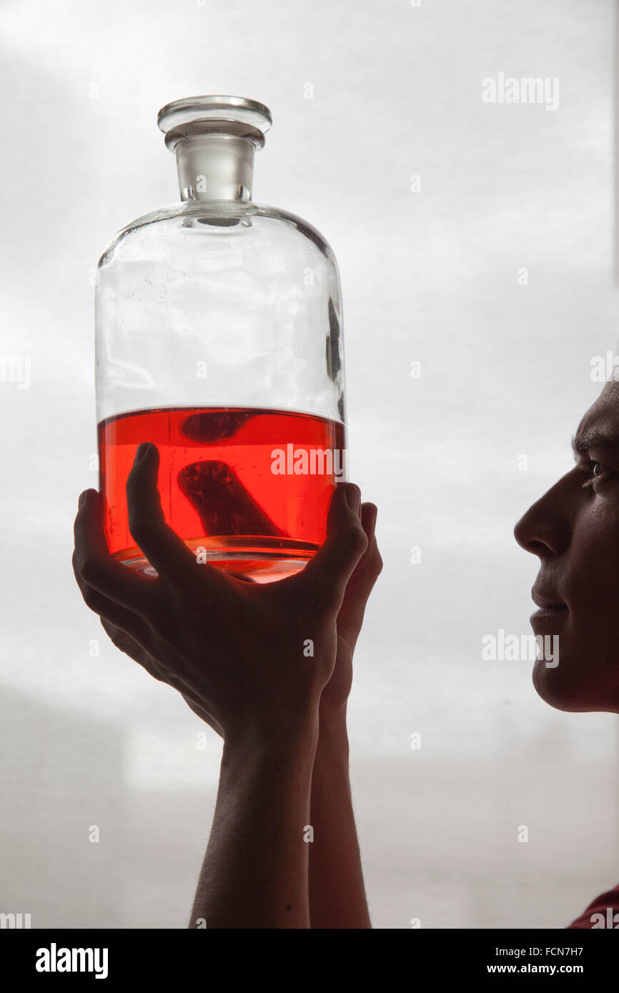 L'homme ressemble un liquide translucide rouge dans un flacon de verre Banque D'Images