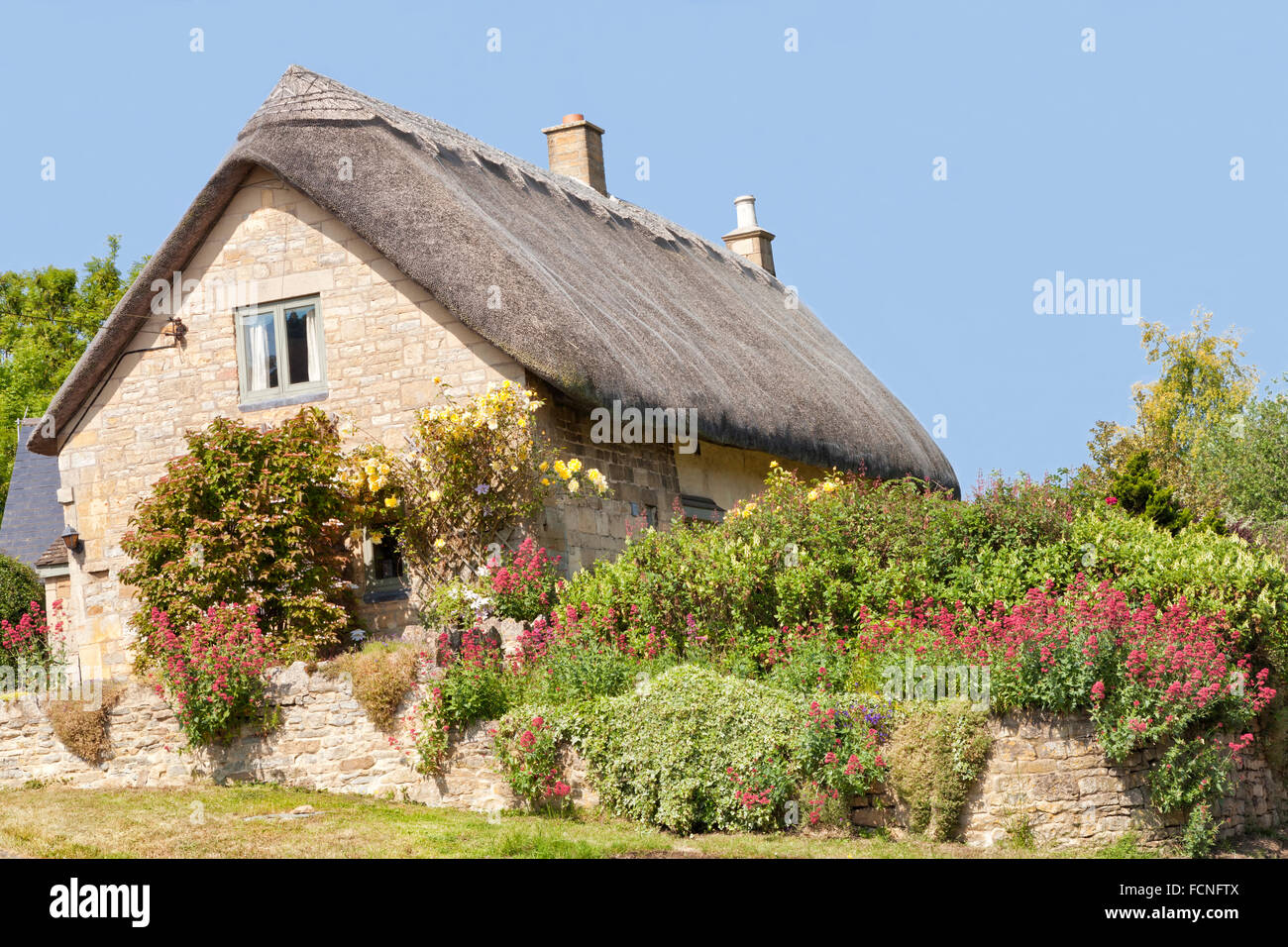 Toit de chaume traditionnel vieux stone Cotswold cottage holiday home avec des roses sur le mur et des fleurs dans le jardin d'été Banque D'Images