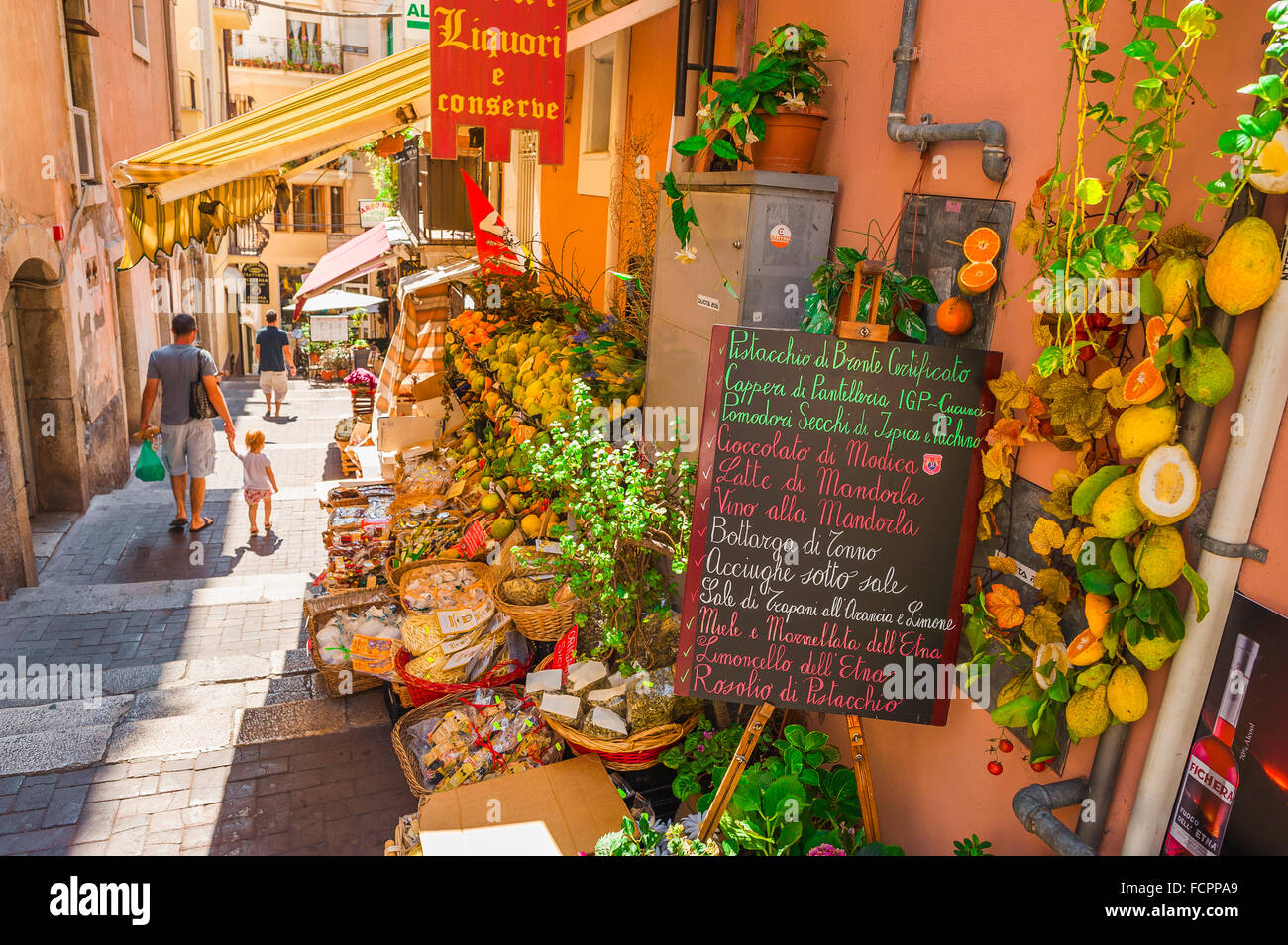 Shopping en famille Italie, un père et un enfant lors d'un voyage shopping passent devant une épicerie colorée dans une rue étroite de Taormina, Sicile, Italie. Banque D'Images