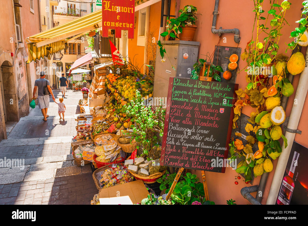 Taormina Sicily, vue d'un parent et d'un enfant passant par une épicerie colorée dans une rue étroite près du Corso Umberto I à Taormina, Sicile. Banque D'Images