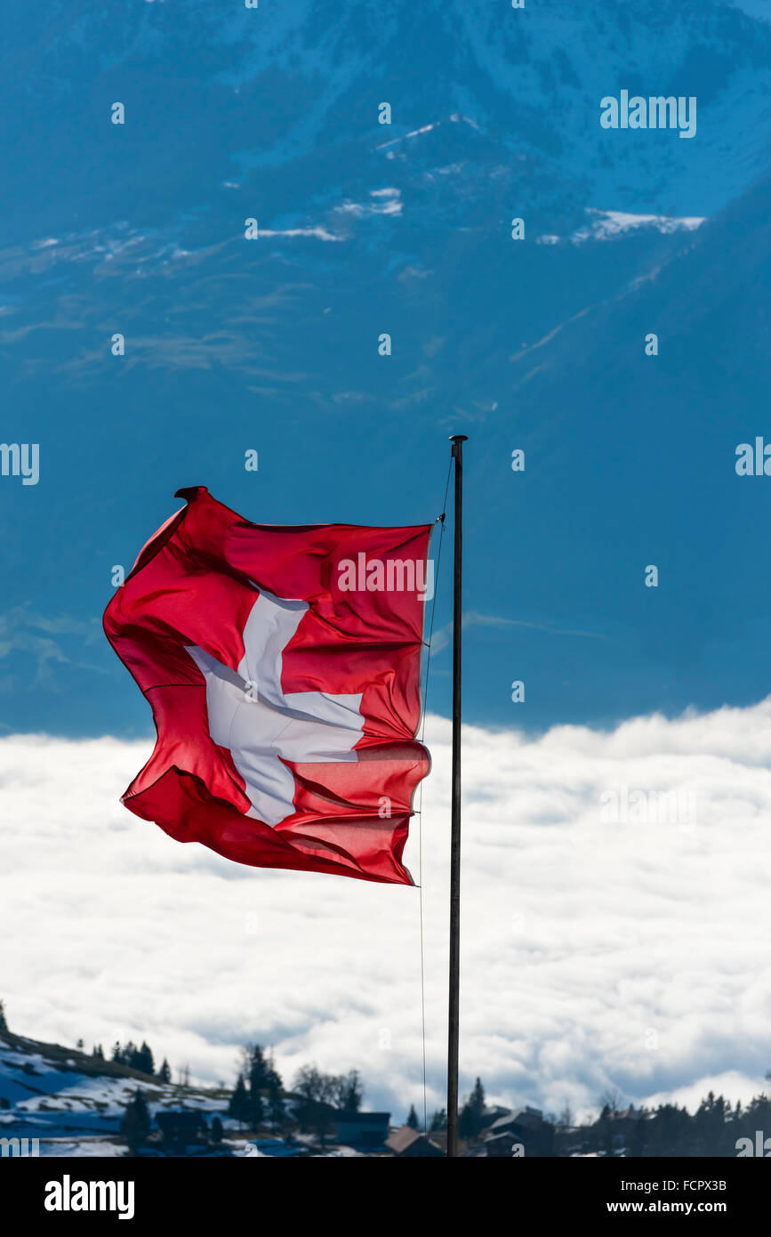 Le drapeau suisse est au vent au-dessus des nuages au sommet du Mont Rigi, Suisse Centrale. Banque D'Images