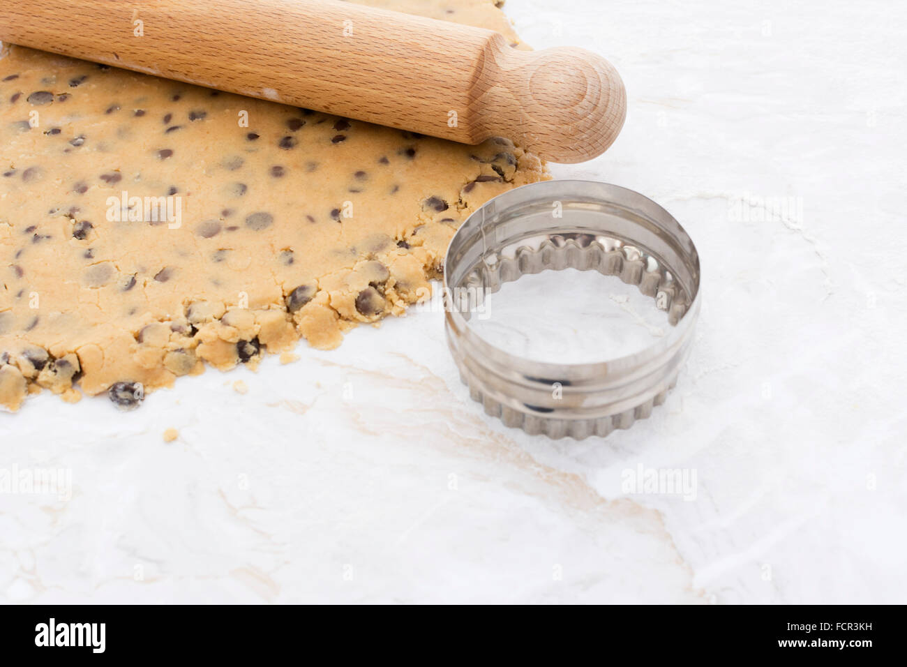 Emporte-pièce circulaire avec la pâte de biscuit aux brisures de chocolat et le rouleau à pâtisserie en bois Banque D'Images