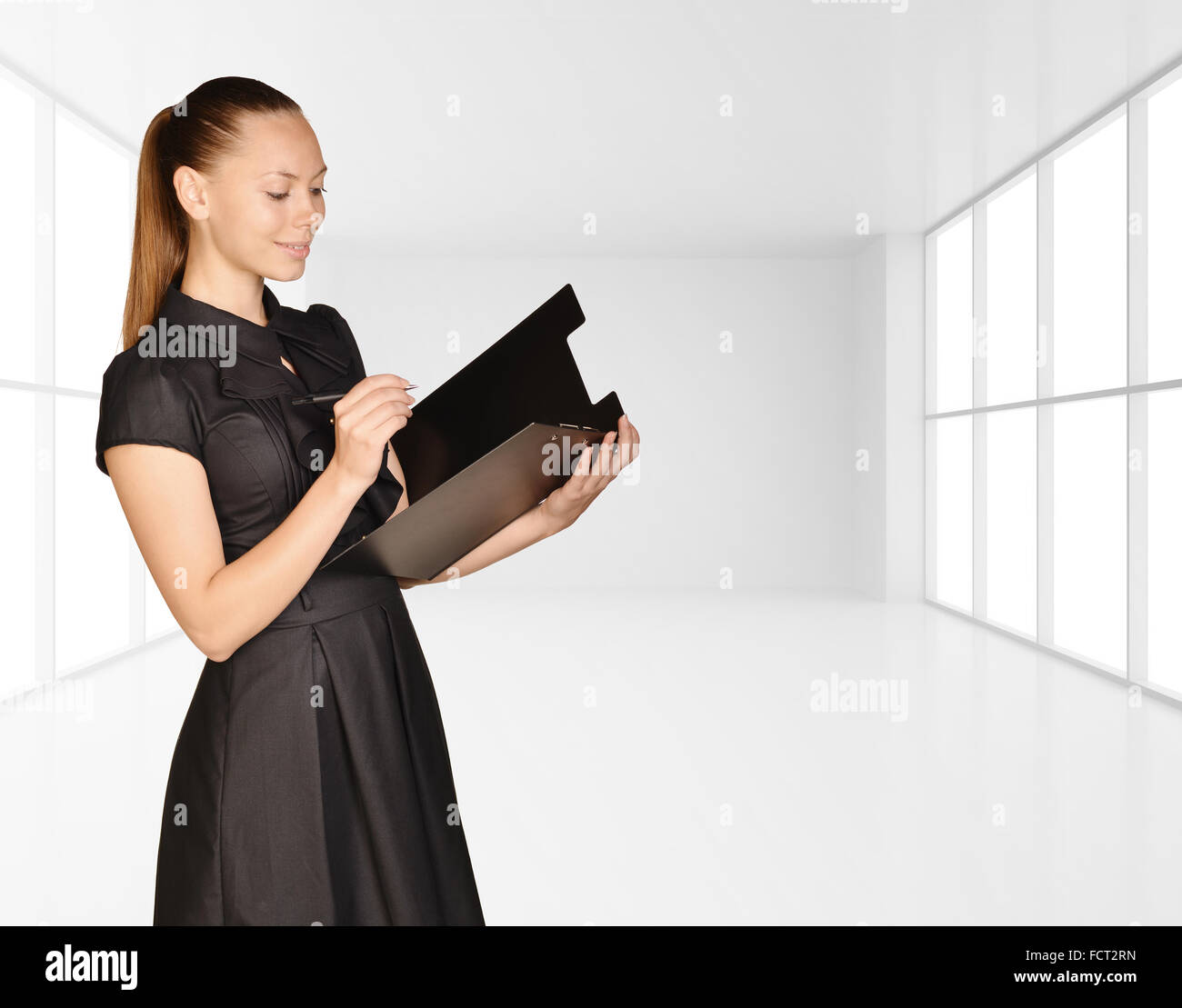 Fille de bureau debout sur fond de lumière intérieur et est holding clipboard Banque D'Images