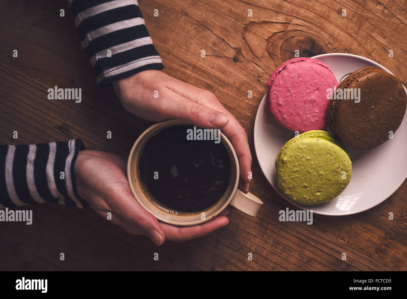 Tasse de café chaud et sucré macaron cookies sur la table le matin, femme hand holding cup avec boisson chaude, vue de dessus, retro Banque D'Images