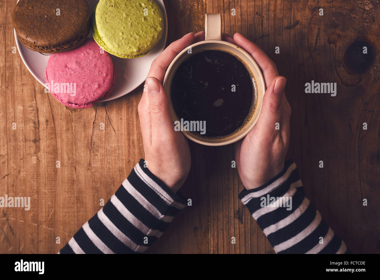 Tasse de café chaud et macaron cookies le matin, femme hand holding cup avec boisson chaude, vue d'en haut, aux couleurs rétro Banque D'Images
