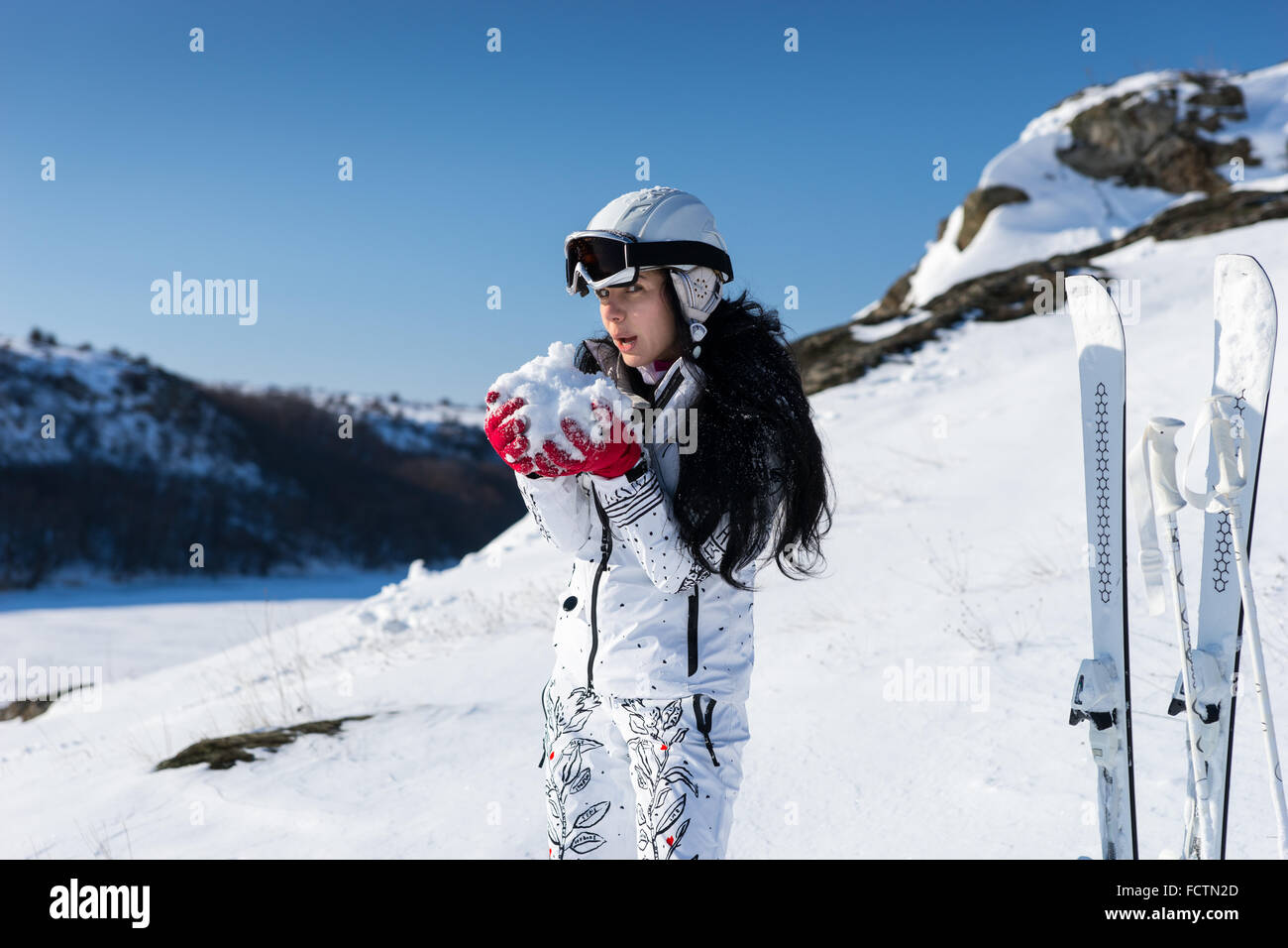 Jeune femme en habit blanc skieur et le casque géant formant boule de neige  en mains comme elle se tient à côté de paire de skis debout Photo Stock -  Alamy