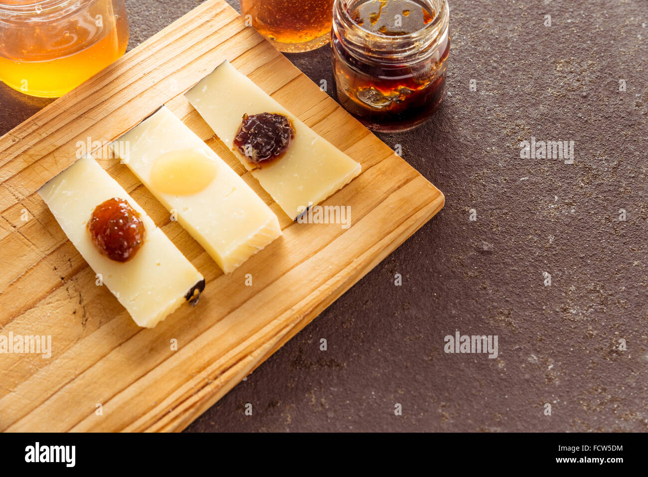 Une composition de tranches de fromage pecorino italien avec des confitures de différentes saveurs sur une planche à découper en bois Banque D'Images
