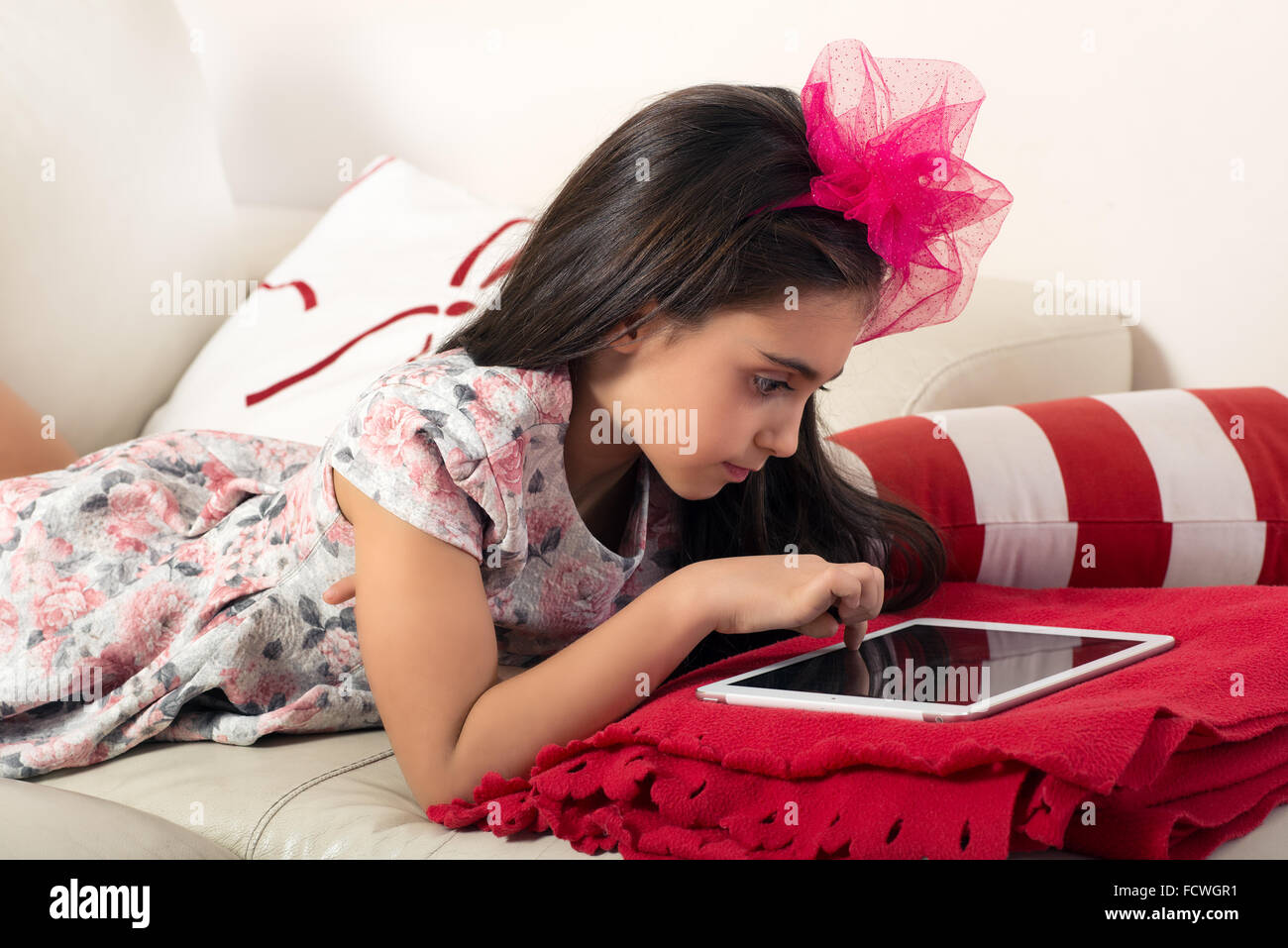 Jeune fille surfer sur l'internet sur une tablette comme elle s'allonge sur son lit sur une couverture rouge avec un ruban assorti dans h Banque D'Images