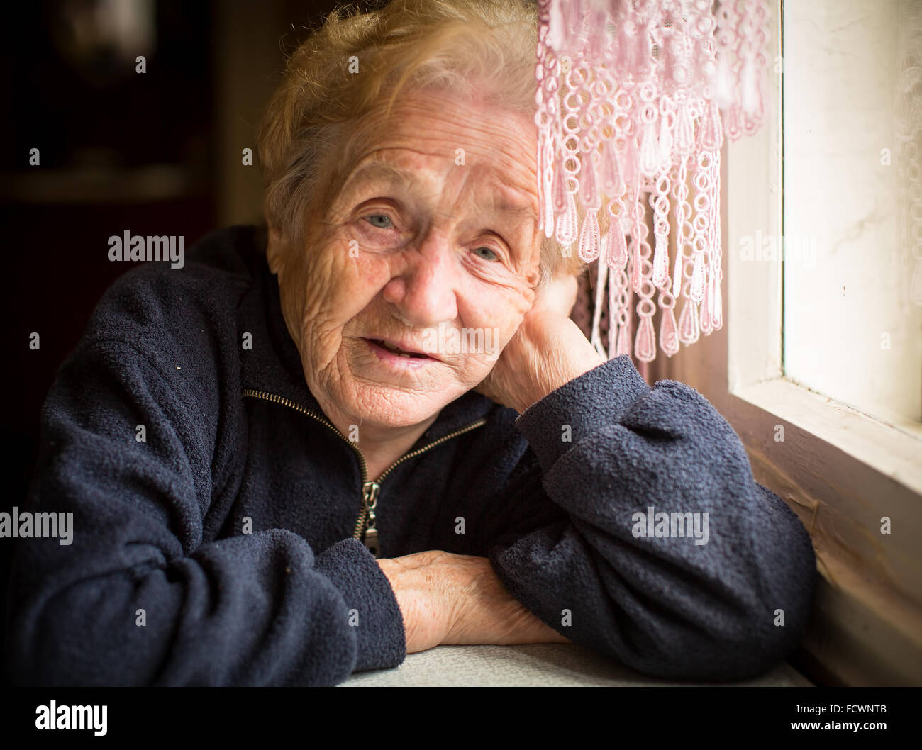 Une vieille femme est assise près de la fenêtre. Banque D'Images
