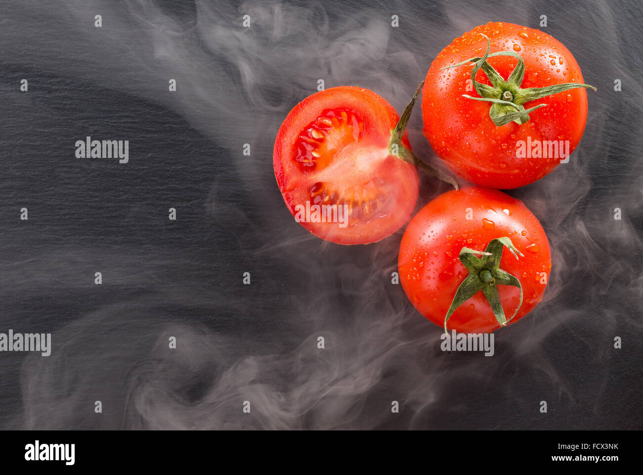 Tomates sur une pierre sombre à la lumière d'arrière-plan de la vapeur. Banque D'Images