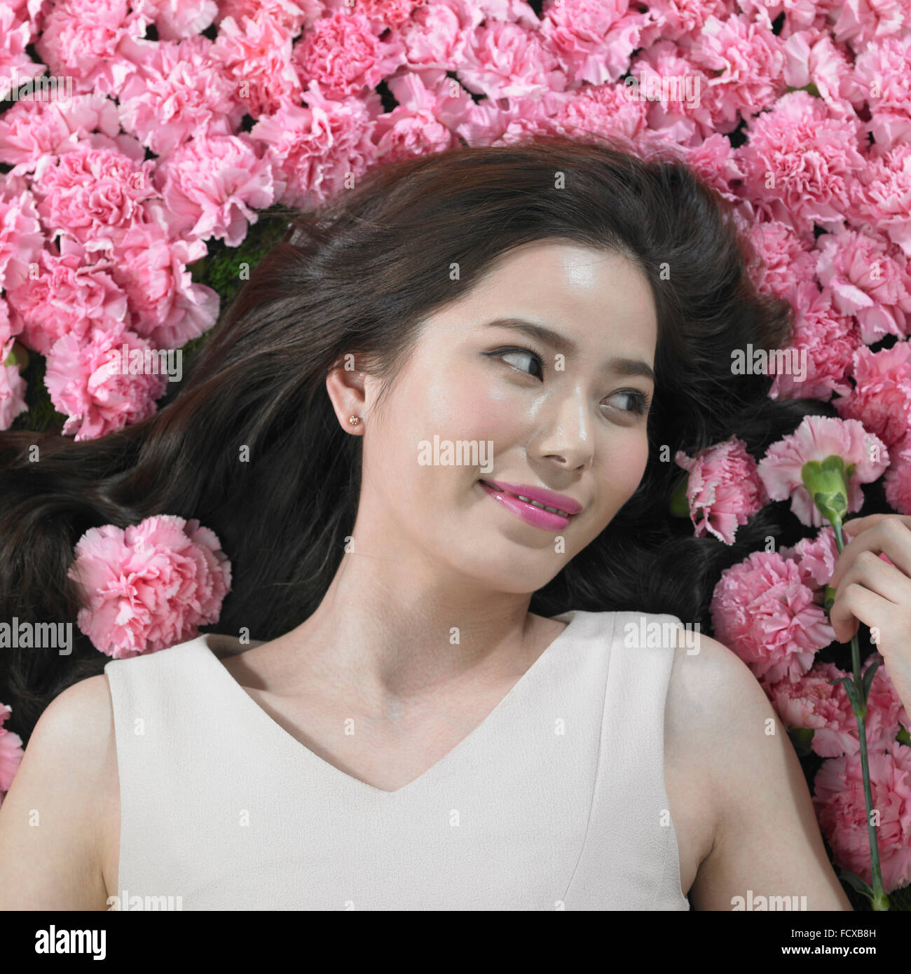 High angle de femme avec de longs cheveux entouré de fleurs et de carnation tenant sur d'entre eux à côté Banque D'Images