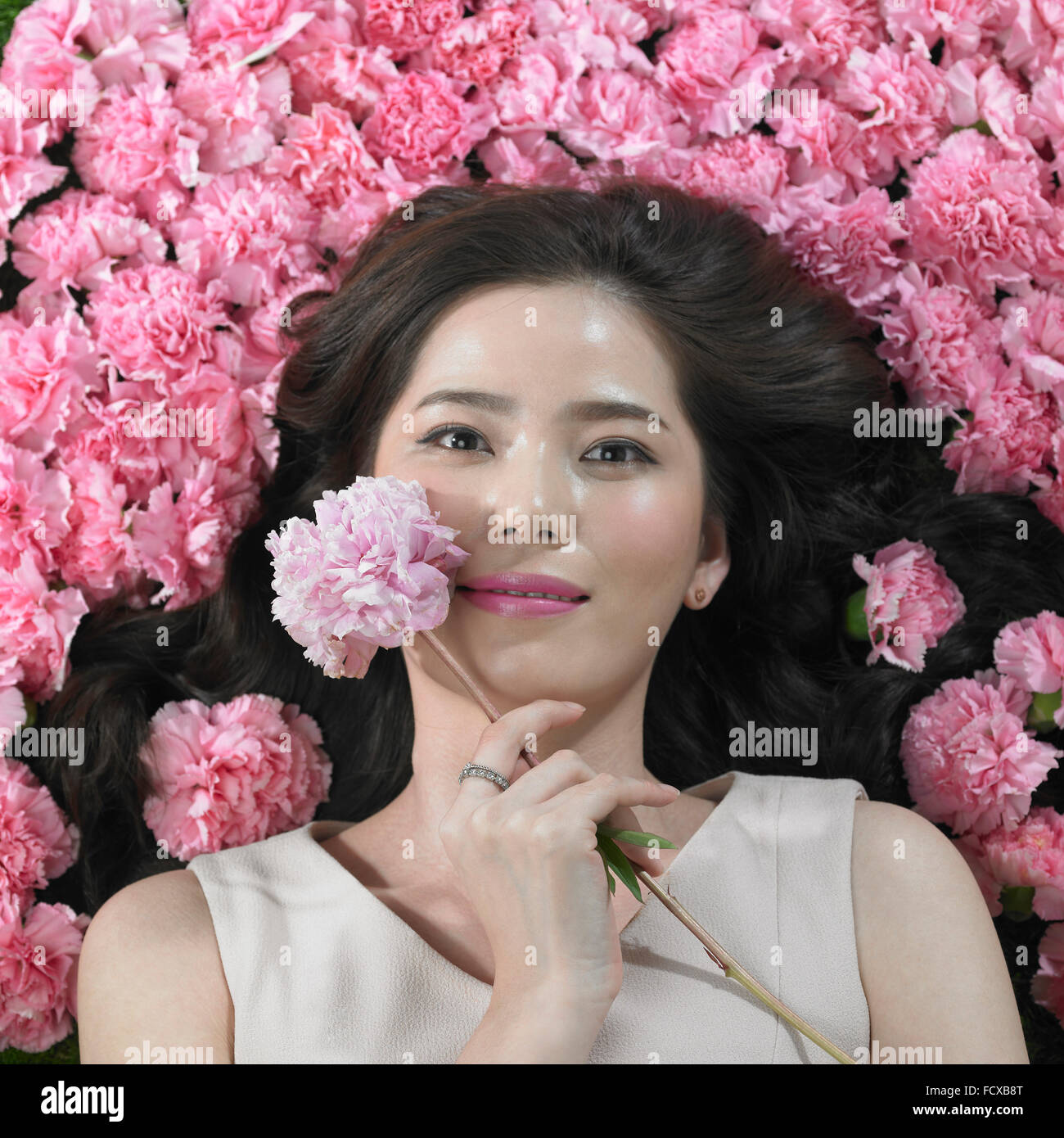 High angle of woman holding Flowers carnation une fleur sur son visage regardant en avant avec un sourire Banque D'Images