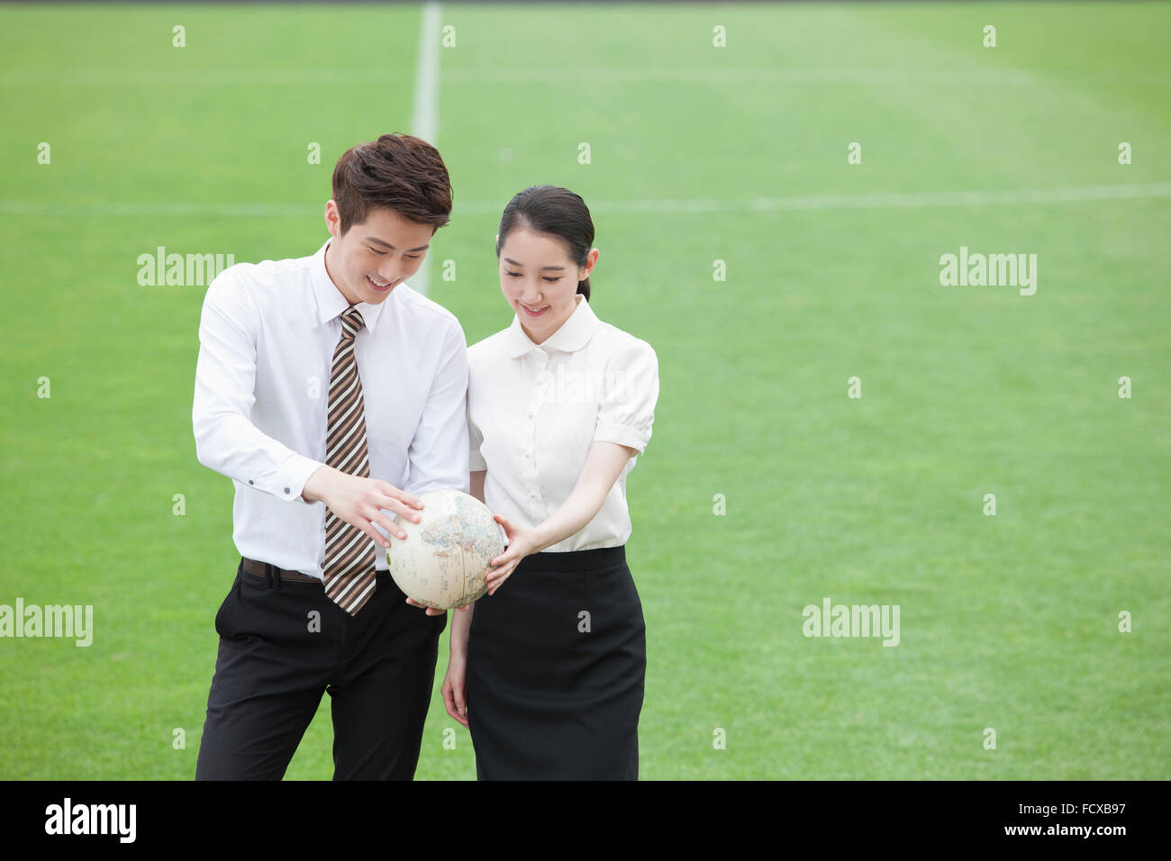 Homme et une femme dans des tenues officielles tenant un globe ensemble et à le regarder avec l'arrière-plan de grass field Banque D'Images