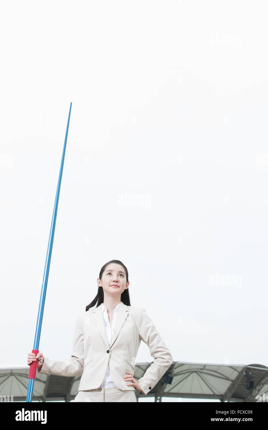 Business Woman holding un pôle pour le saut de l'autre main sur sa taille et à regarder avec l'arrière-plan de terrain de sport Banque D'Images