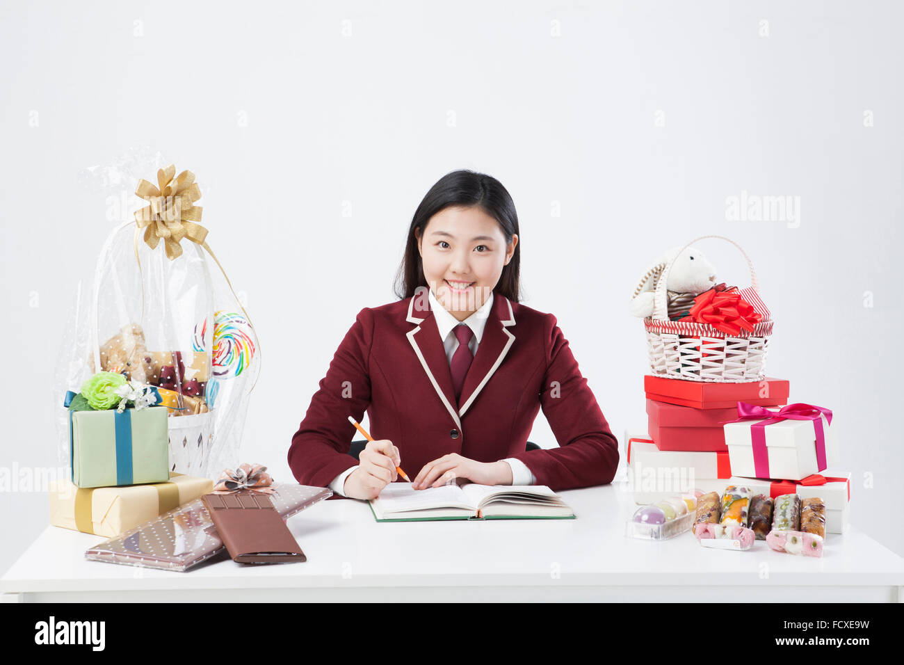 High school girl assis à un bureau avec un livre autour de nombreux cadeaux Banque D'Images