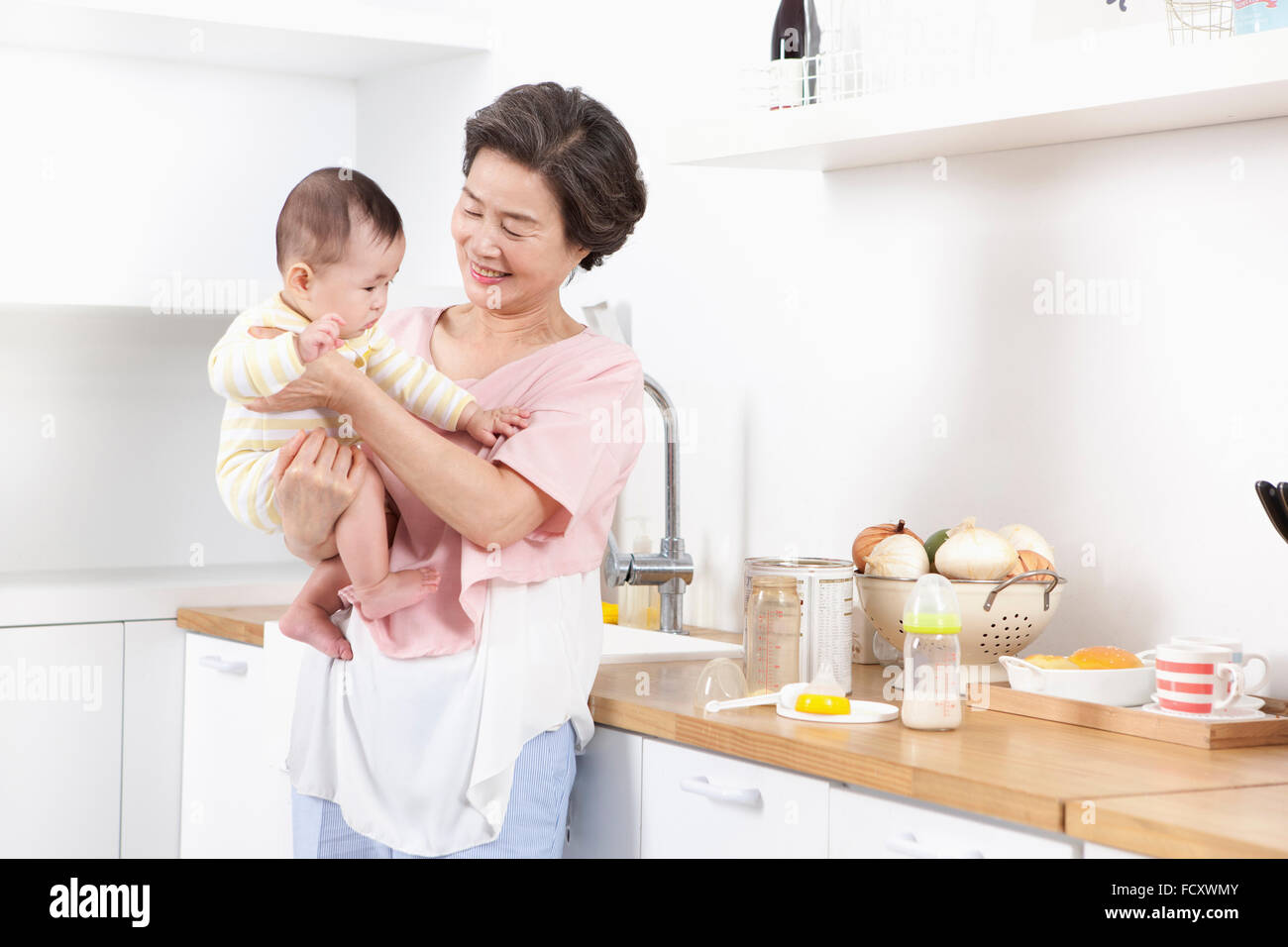 Vieille Femme jouant avec un bébé dans la cuisine Banque D'Images