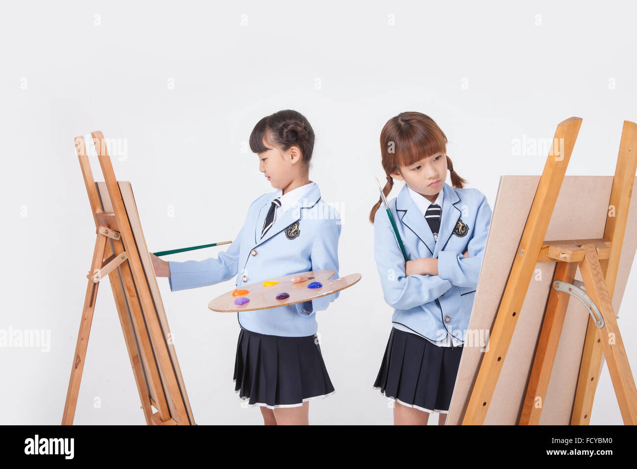 Fille de l'école élémentaire du dessin avec les outils de dessin et de l'autre fille regardant un chevalet avec ses bras croisés tant à l'école Banque D'Images