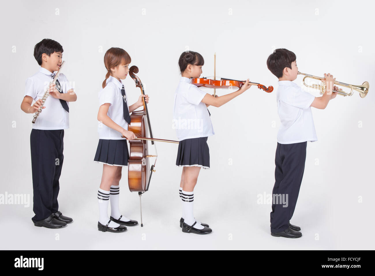 Quatre étudiants du primaire en uniforme se tenant dans la ligne et de la lecture d'un instrument de musique classique chaque Banque D'Images