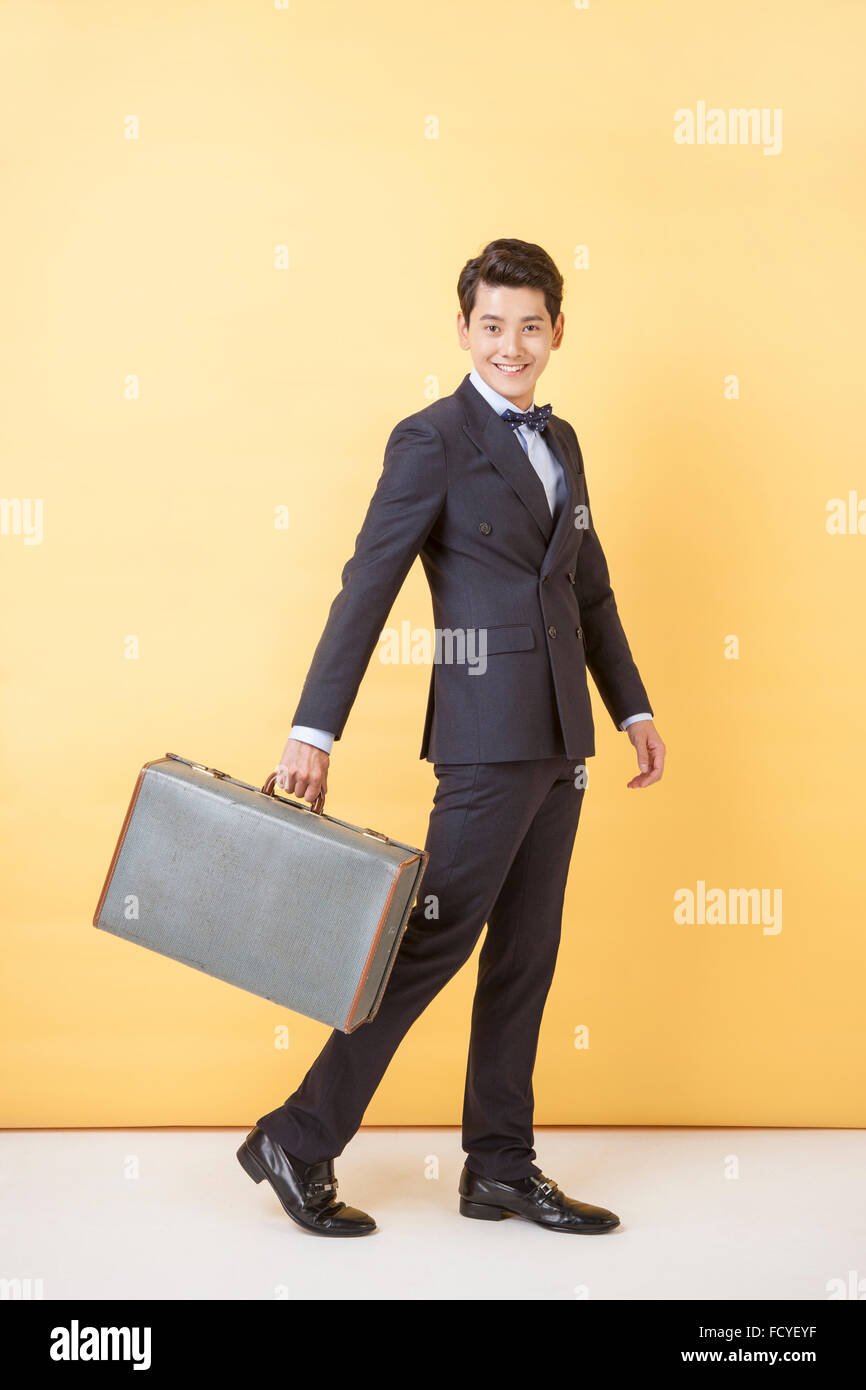 L'homme en costume et nœud papillon marcher avec une valise fixant l'avant avec un sourire Banque D'Images