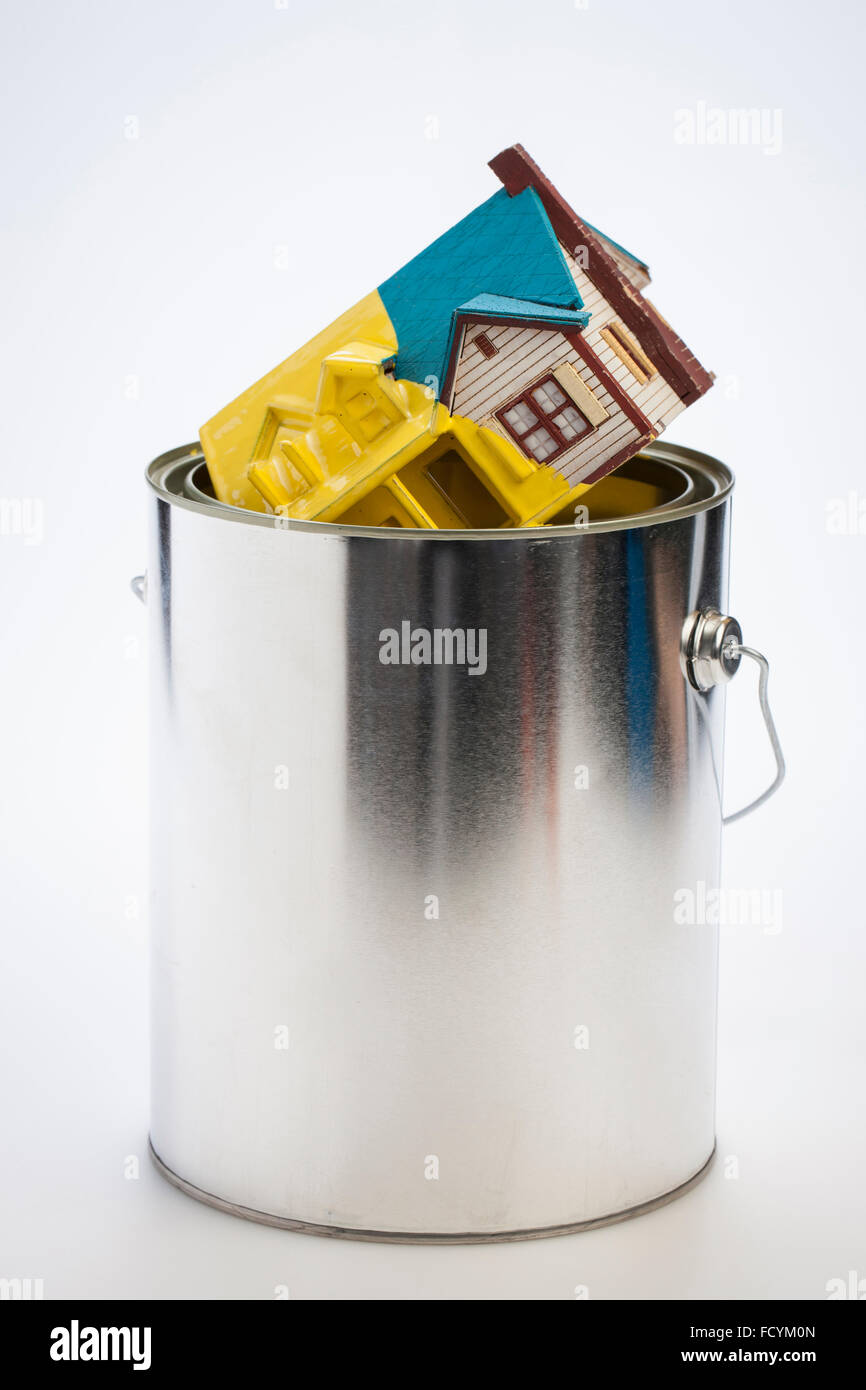 Maison miniature dégoulinant de peinture jaune à partir d'un pot de peinture Banque D'Images