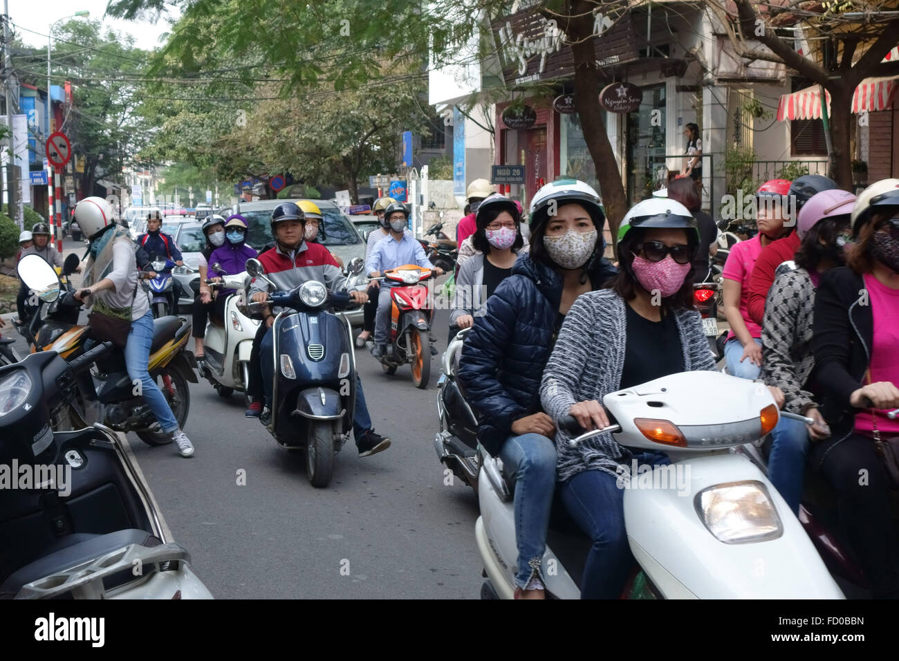 Des scooters avec cavaliers, certains portant des masques, dans une rue animée de Hanoi, Vietnam Banque D'Images