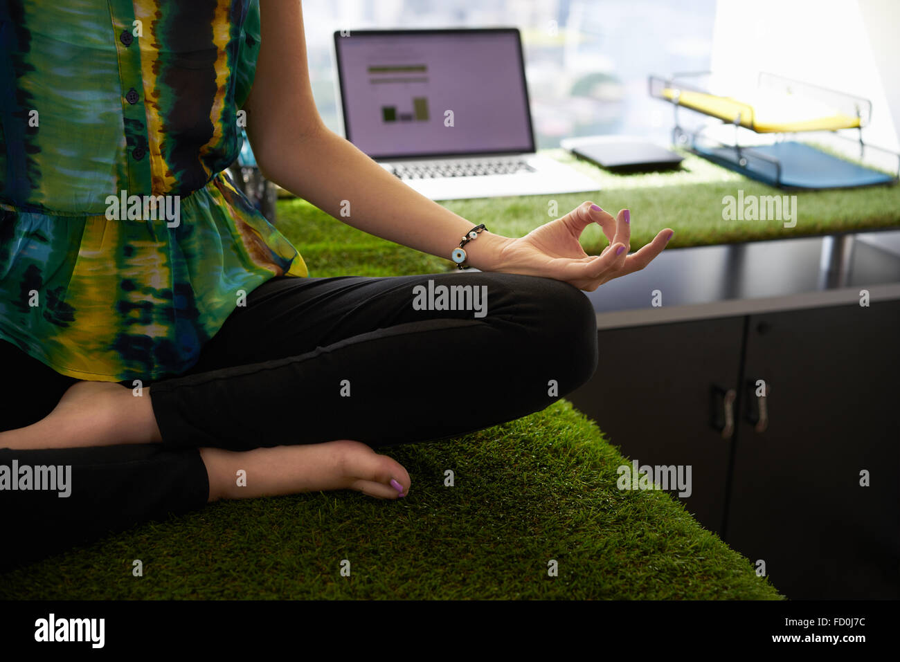 Young hispanic woman in office, assis sur 24 couverts d'herbe et de plantes. Elle médite yoga Yoga en position du lotus. Vie rognée Banque D'Images