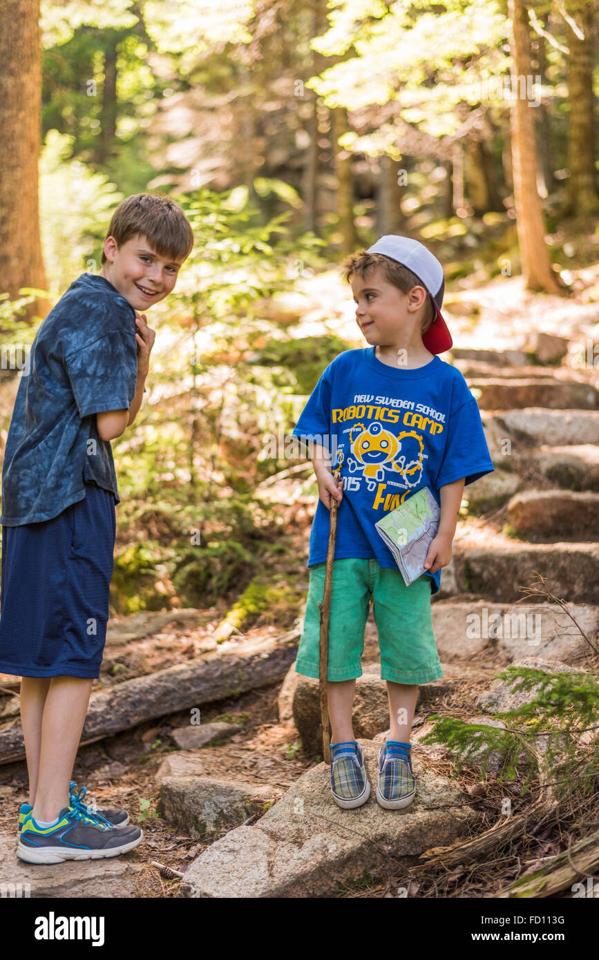 Un garçon de 5 ans est titulaire de la carte et un bâton de marche sur une randonnée en famille dans l'Acadia National Park. Il est souriant à son grand frère. Banque D'Images