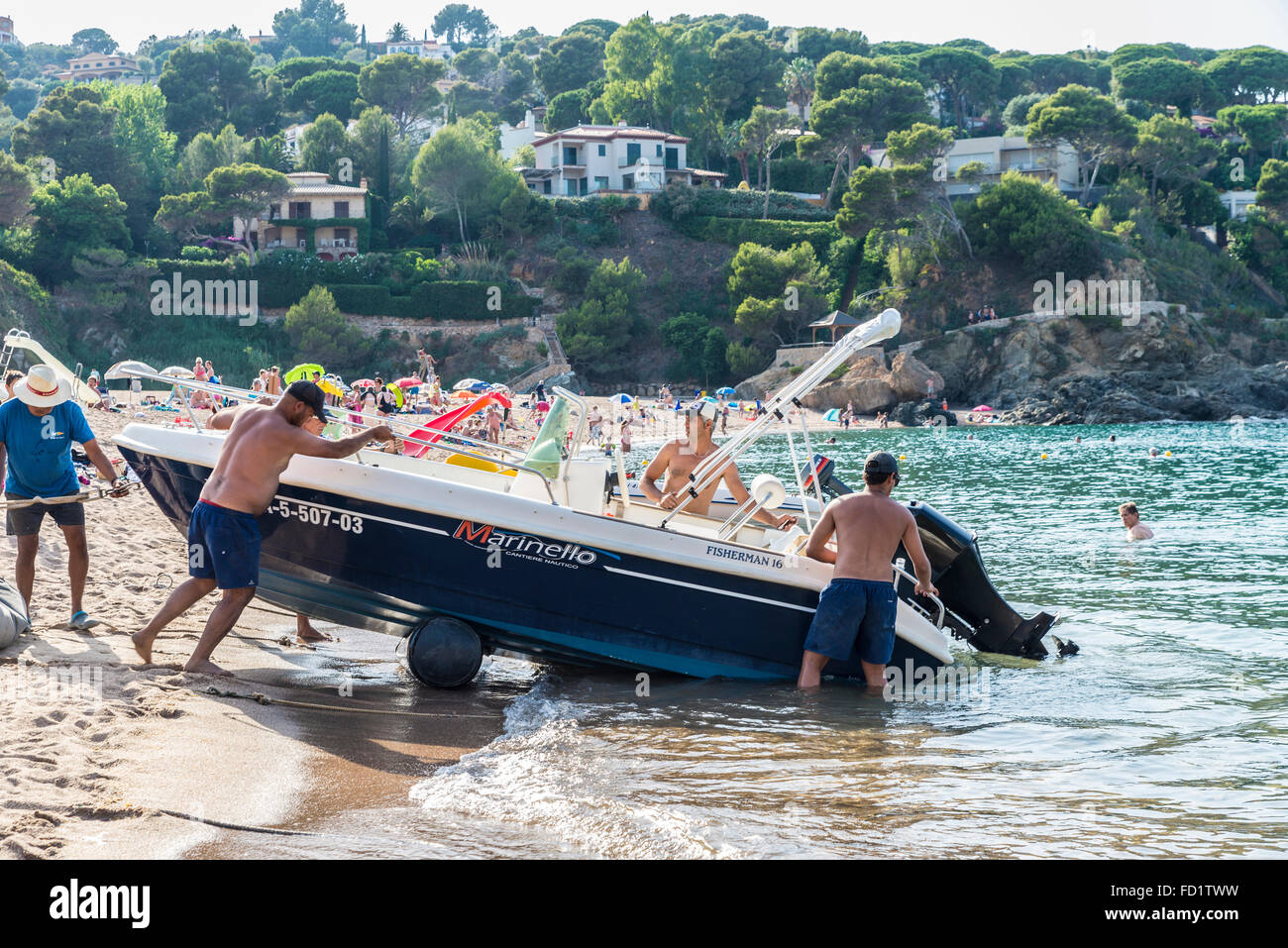 Plusieurs hommes poussant un bateau sur la plage en place dans la plage de Sa Riera de la Costa Brava, Catalogne, Espagne Banque D'Images