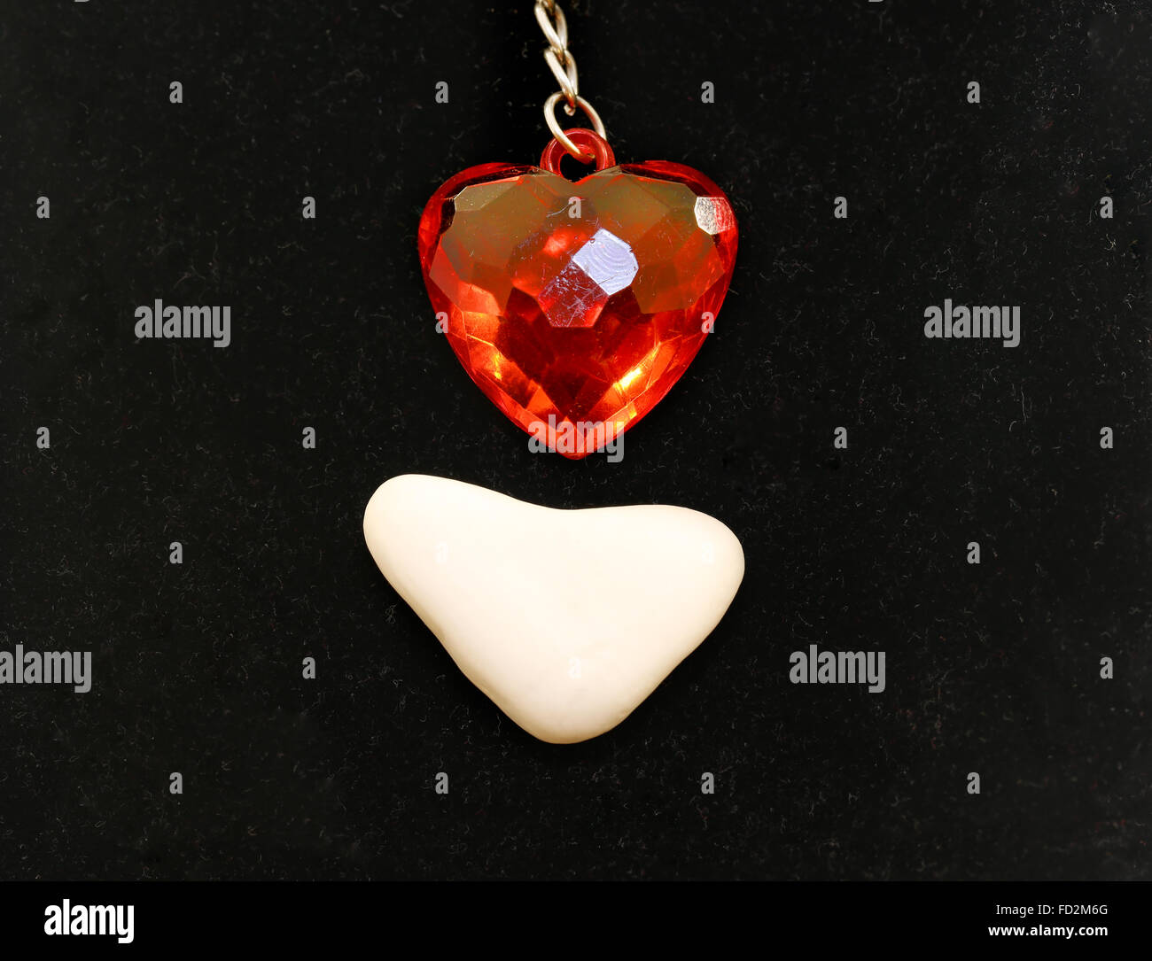 Coeur rouge en plastique et une pierre blanche en forme de cœur photographié close up sur fond noir Banque D'Images