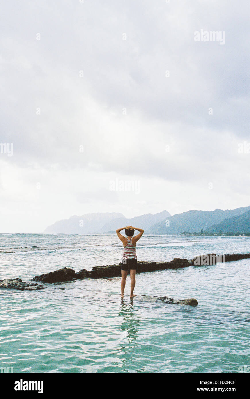 Portrait d'une femme debout sur des rochers avec son dos à la caméra dans l'eau dans Oahu Hawaii. Banque D'Images