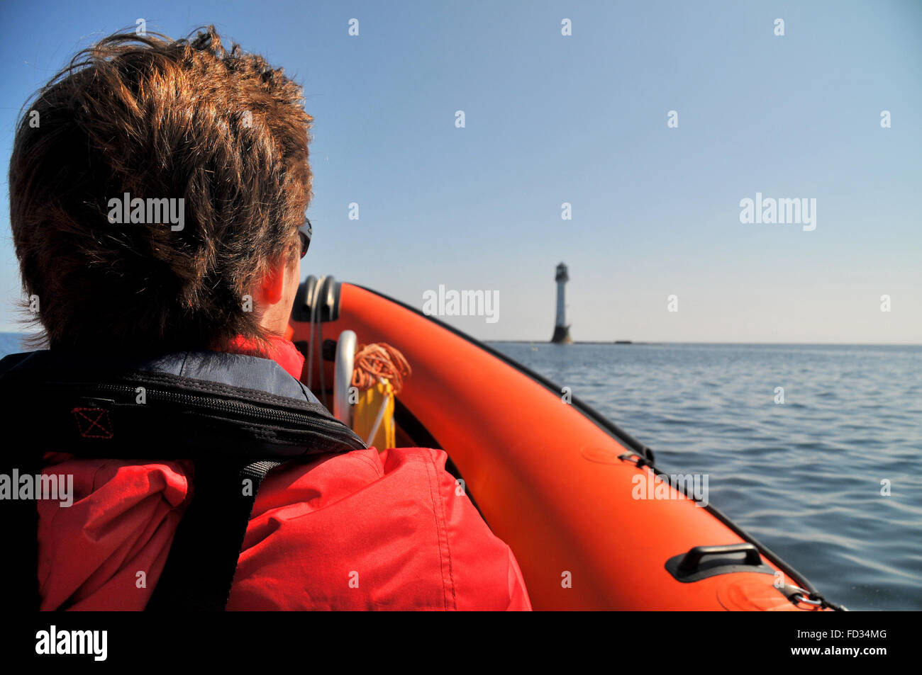 Un jeune homme voyageant sur un bateau gonflable rigide s'approche du phare de Bell Rock, au large de la côte d'Angus en Écosse. Banque D'Images
