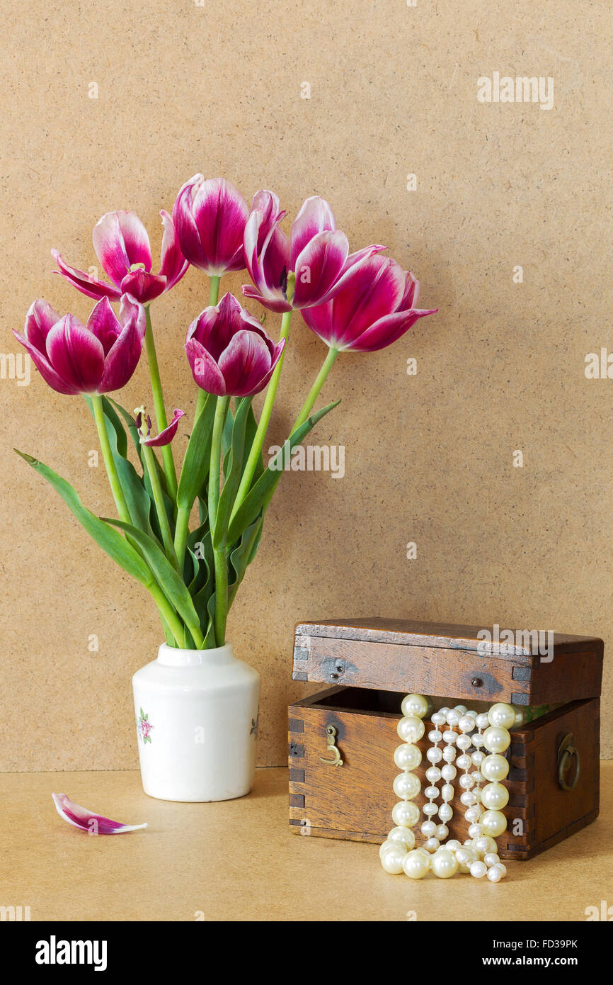 Violet vif des fleurs dans un vase blanc tulipes et coffre en bois avec des perles Banque D'Images