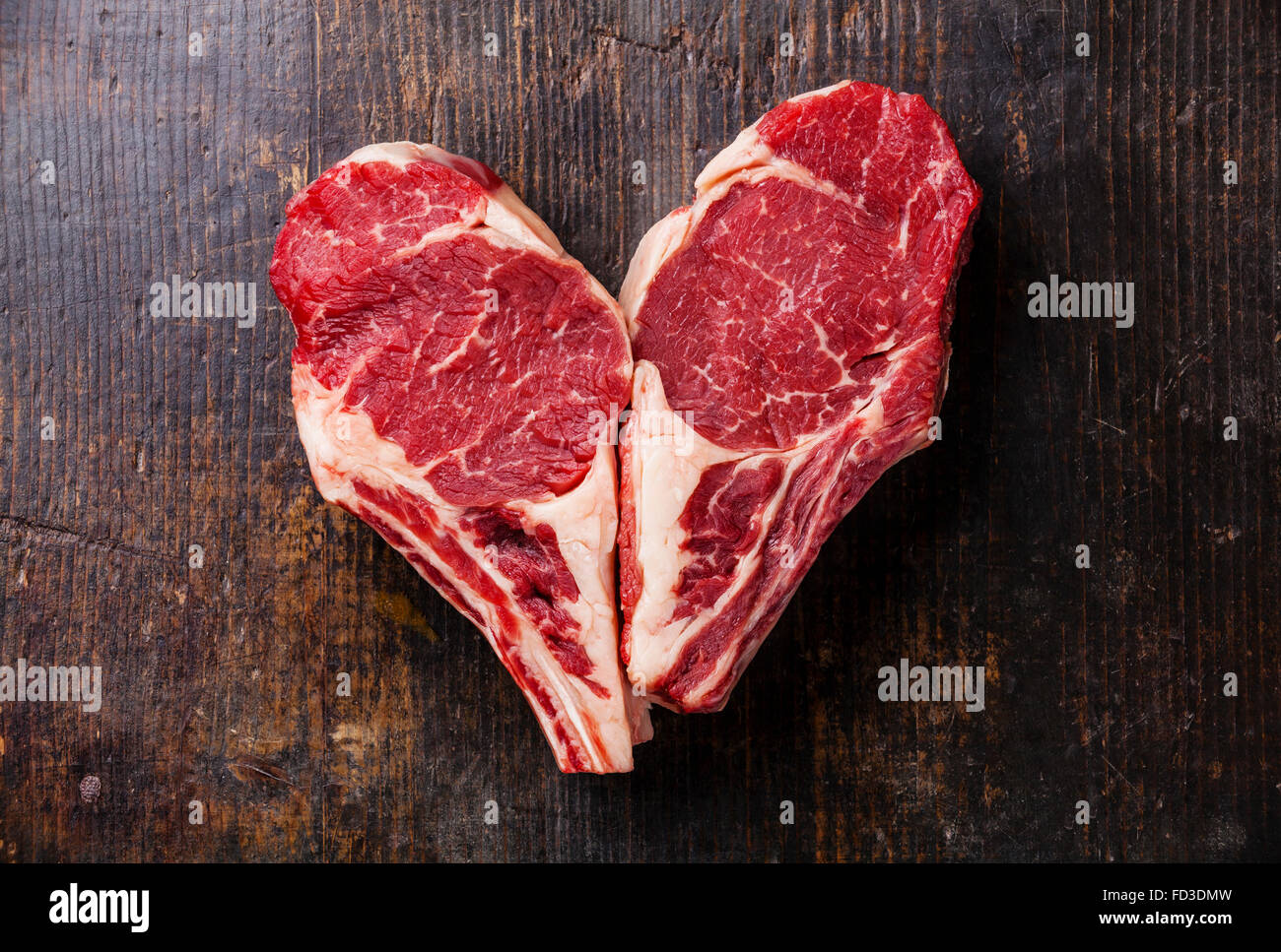 Forme de coeur la viande crue Ribeye Steak entrecote sur l'os sur fond de bois Banque D'Images