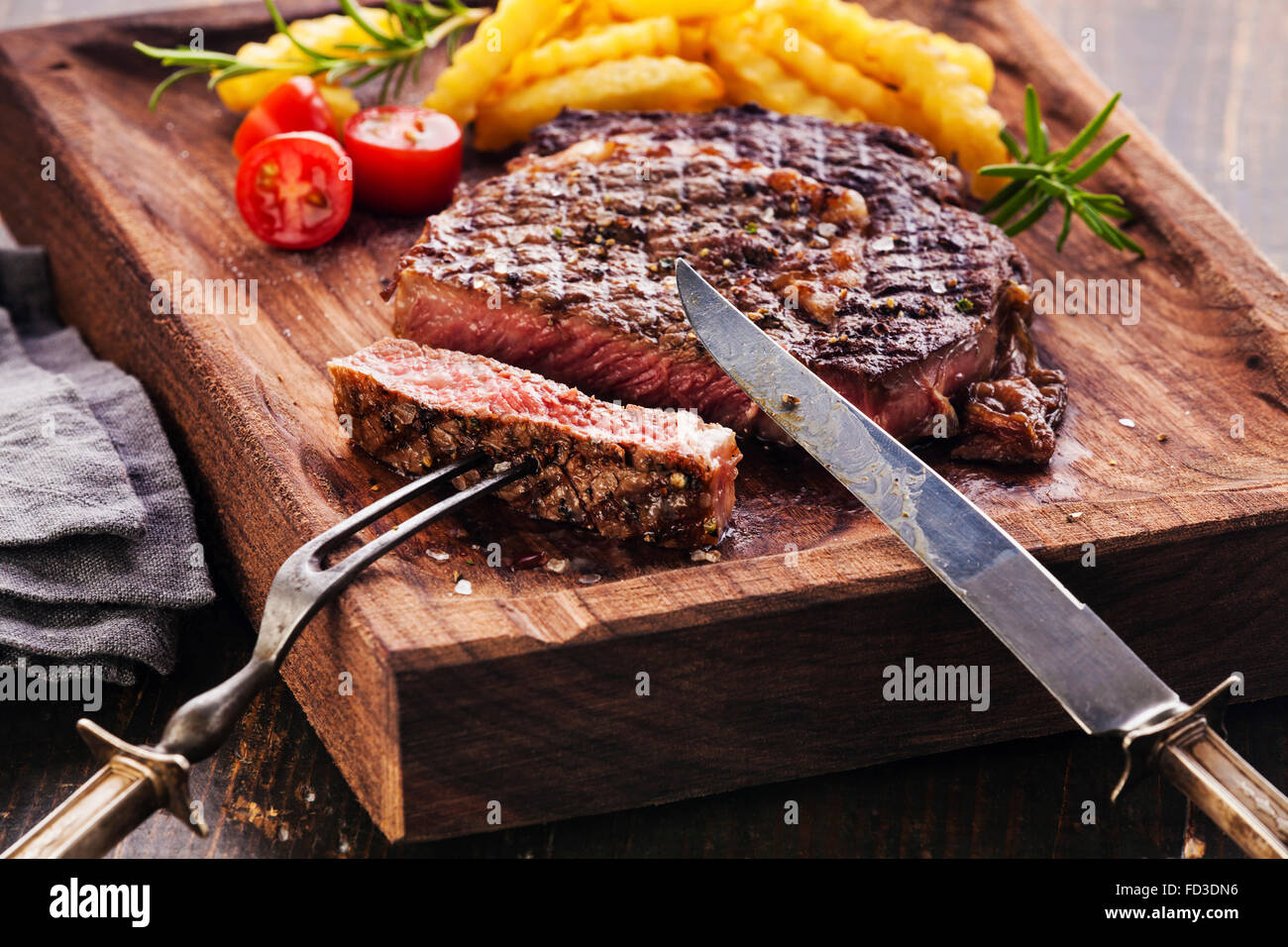 Tranches de steak Ribeye avec frites sur le service à bord bloc sur fond de bois Banque D'Images Tranches de steak Ribeye avec frites sur le service à bord bloc sur fond de bois Banque D'Images