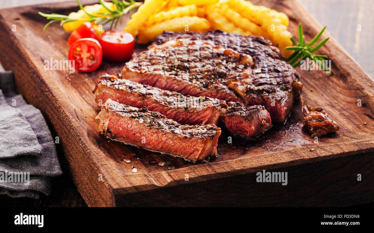 Tranches de steak Ribeye avec frites sur le service à bord bloc sur fond de bois Banque D'Images Tranches de steak Ribeye avec frites sur le service à bord bloc sur fond de bois Banque D'Images