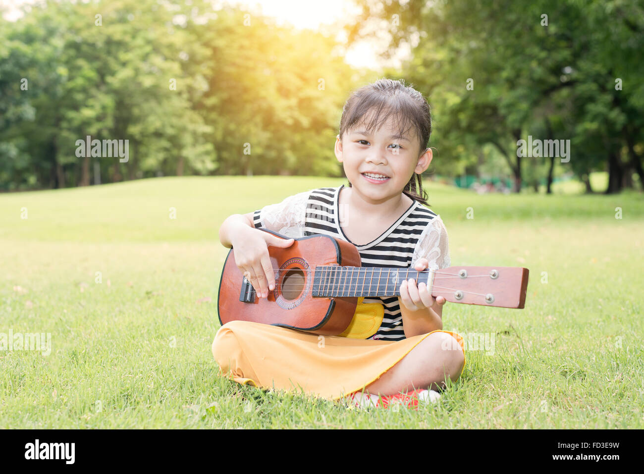 Petite fille asiatique assis sur l'herbe et jouer ukulele in park Banque D'Images