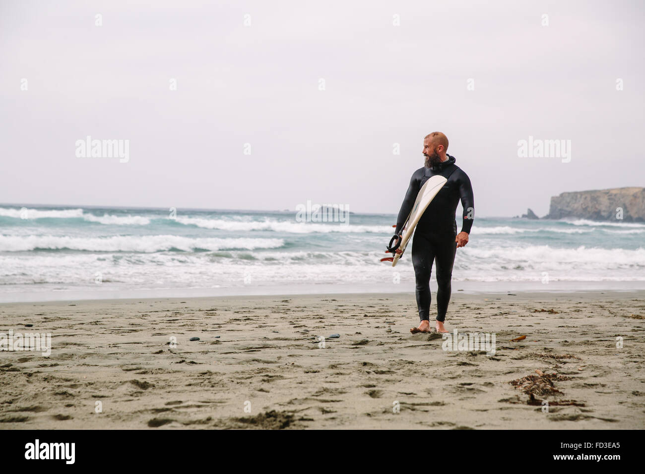Un surfeur promenades dans de l'eau après une journée sur les vagues à Big Sur, en Californie. Banque D'Images