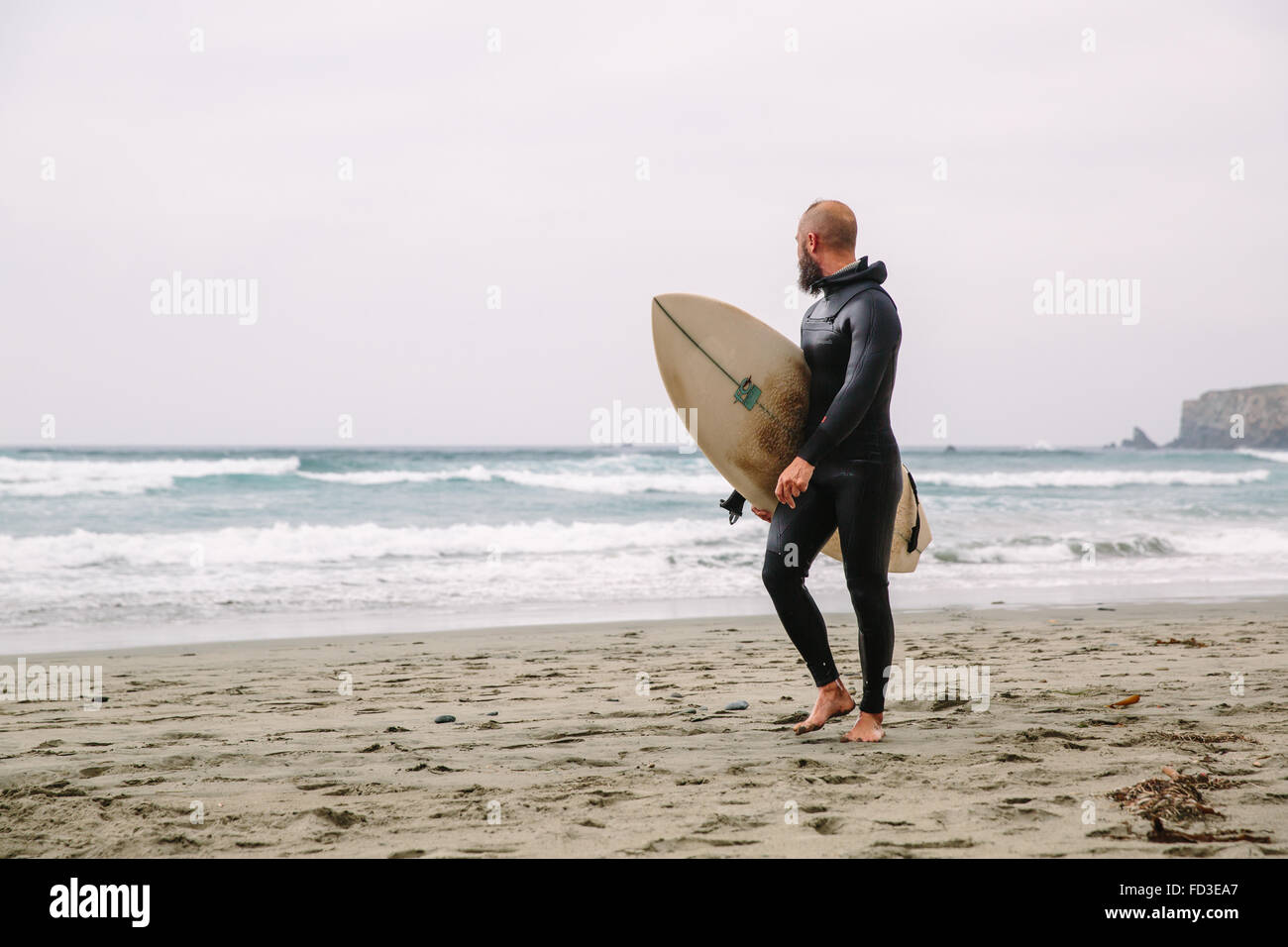 Un surfeur promenades dans de l'eau après une journée sur les vagues à Big Sur, en Californie. Banque D'Images