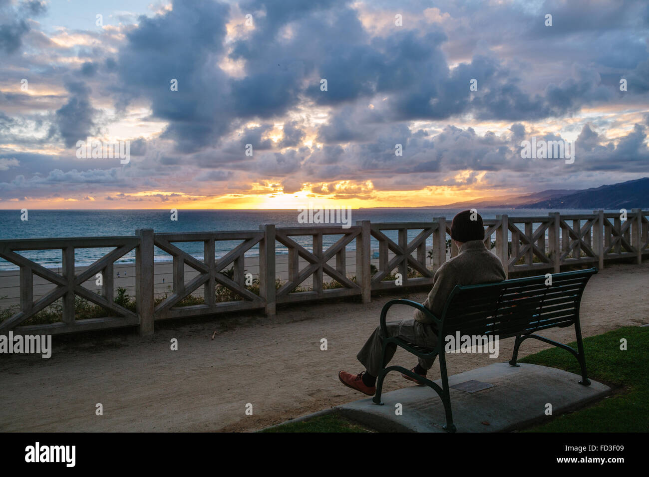 Un homme est assis sur un banc de parc avec vue sur le coucher du soleil sur l'océan. Santa Monica, Californie. Banque D'Images