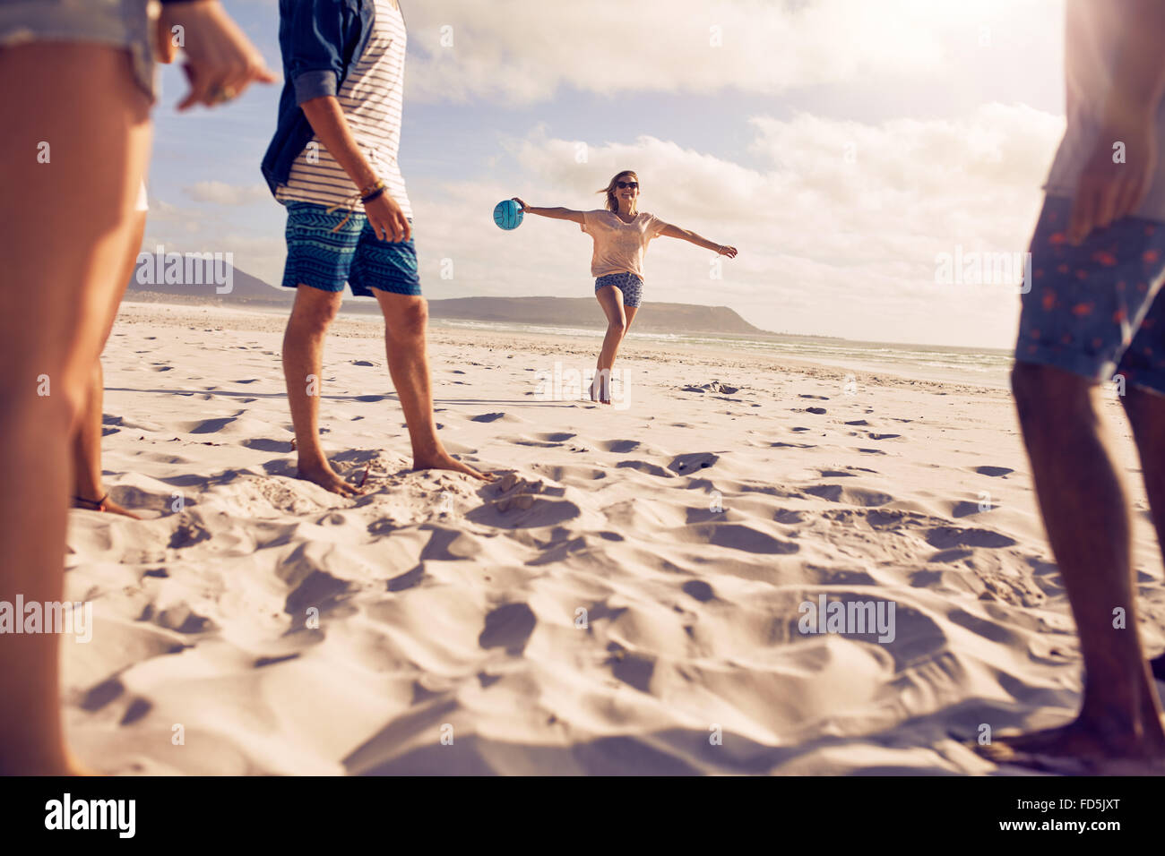 Low angle view of young woman running sur la plage avec un ballon avec ses amis debout devant. Groupe d'amis profitant de hol Banque D'Images