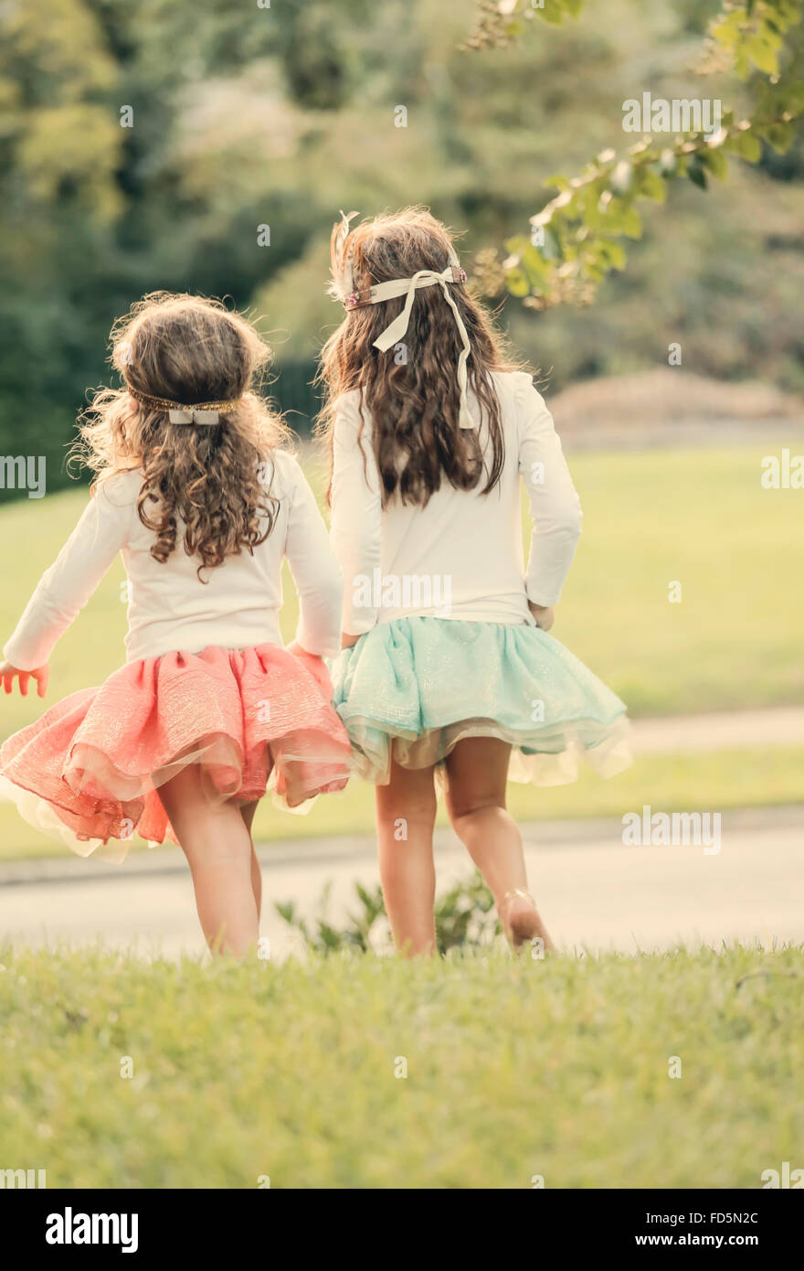 Deux jeunes filles portant tutu's marcher dans l'herbe de l'appareil photo. Banque D'Images