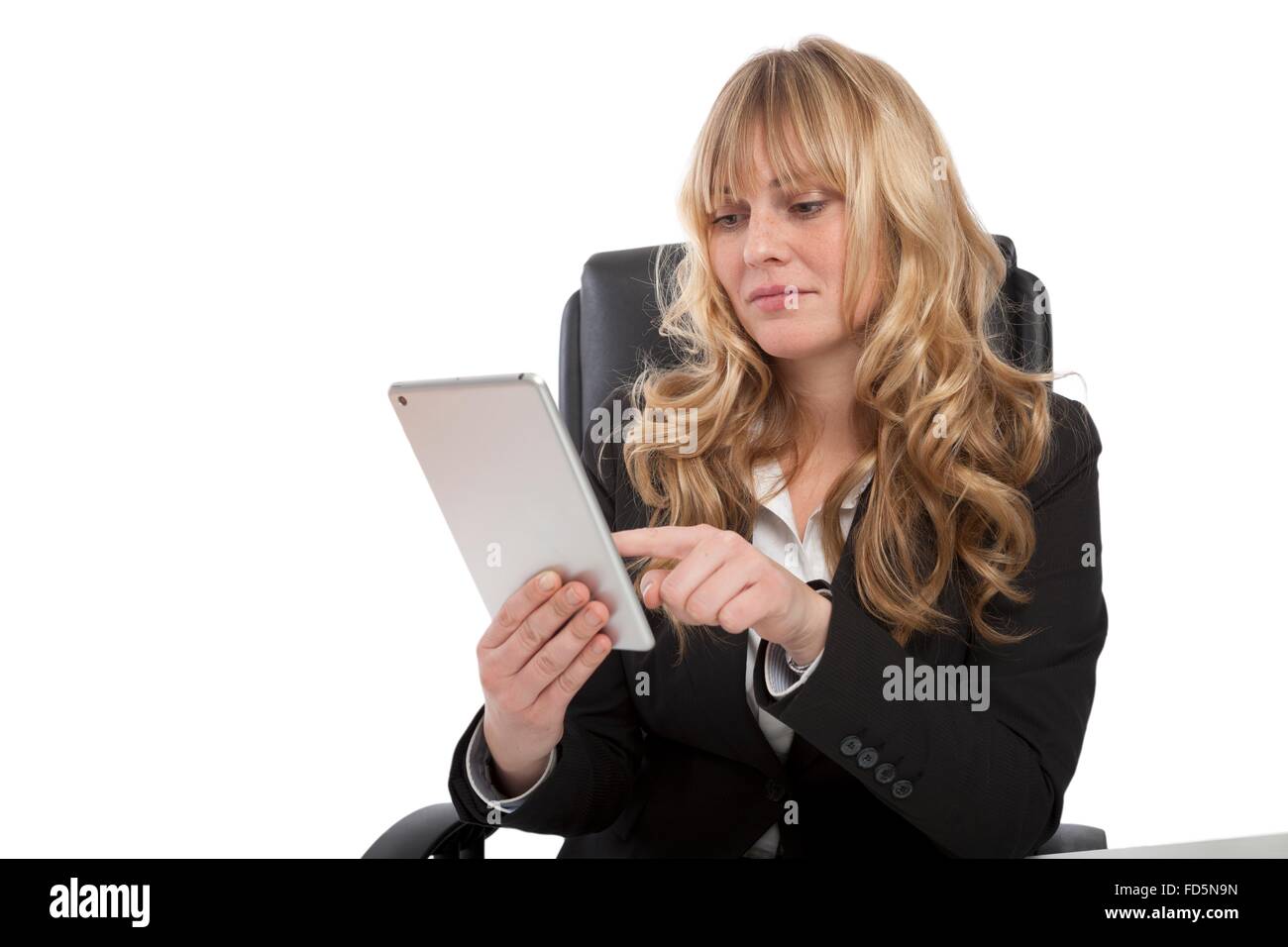 Smiling young businesswoman sitting at her desk en utilisant sa tablette pour surfer sur internet comme elle s'occupe de ses affaires au quotidien Banque D'Images