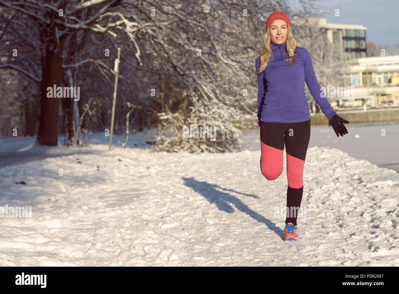 Jeune femme active l'exercice en plein air dans un parc à neige de l'hiver blanc frais faisant des exercices d'étirement pour réchauffer comme elle sourit Banque D'Images