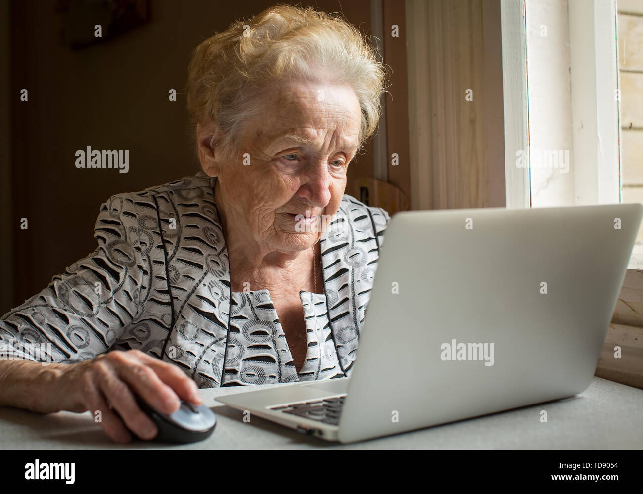 Une femme âgée assise à la table et les types sur ordinateur portable. Banque D'Images