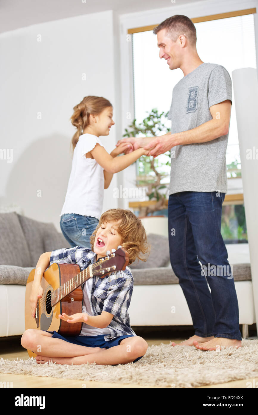 Garçon jouant de la guitare et de père et la soeur de danse à la musique à la maison Banque D'Images