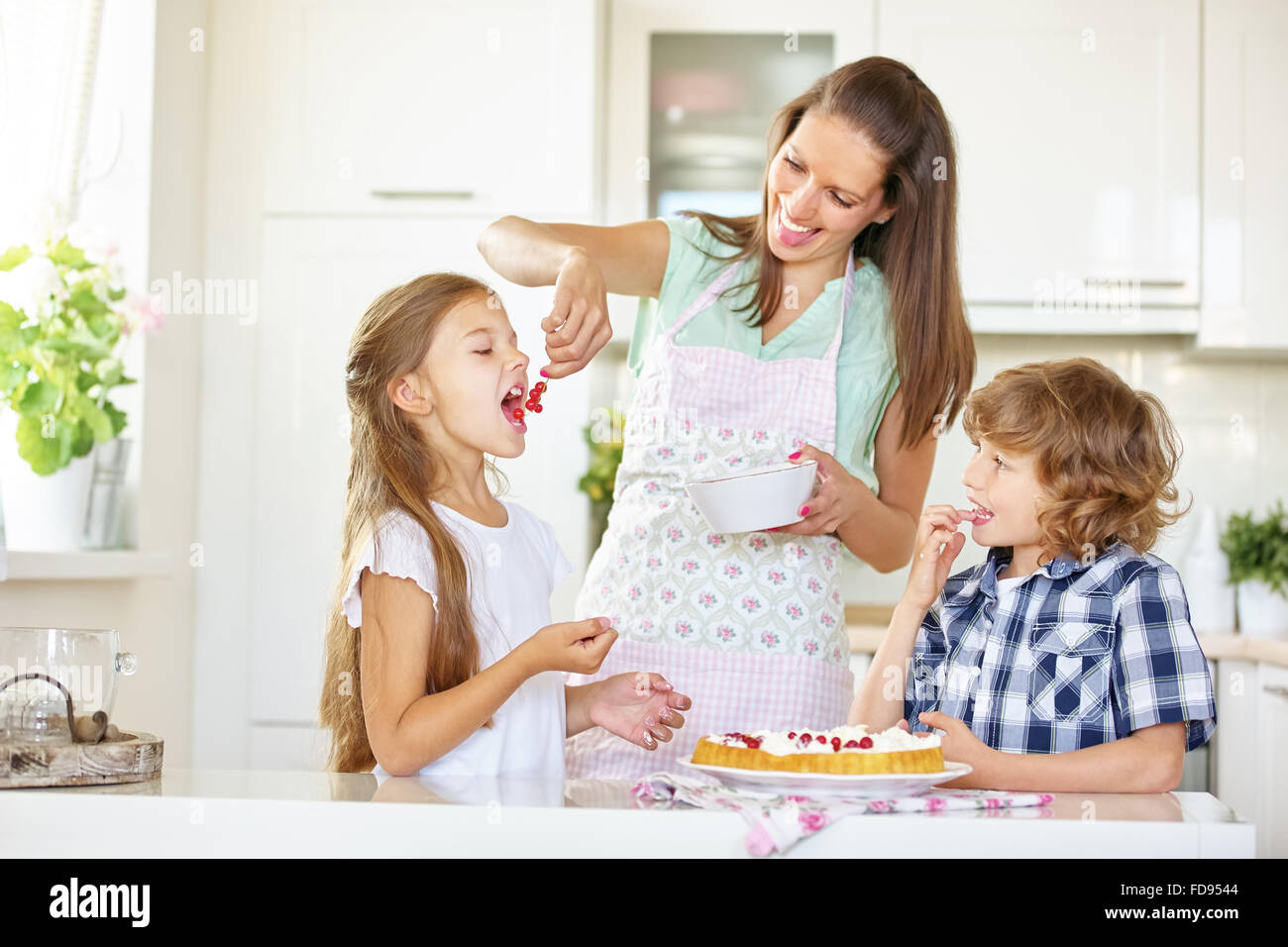 Mère et enfants gâteau à pâte avec groseilles rouges dans la cuisine Banque D'Images
