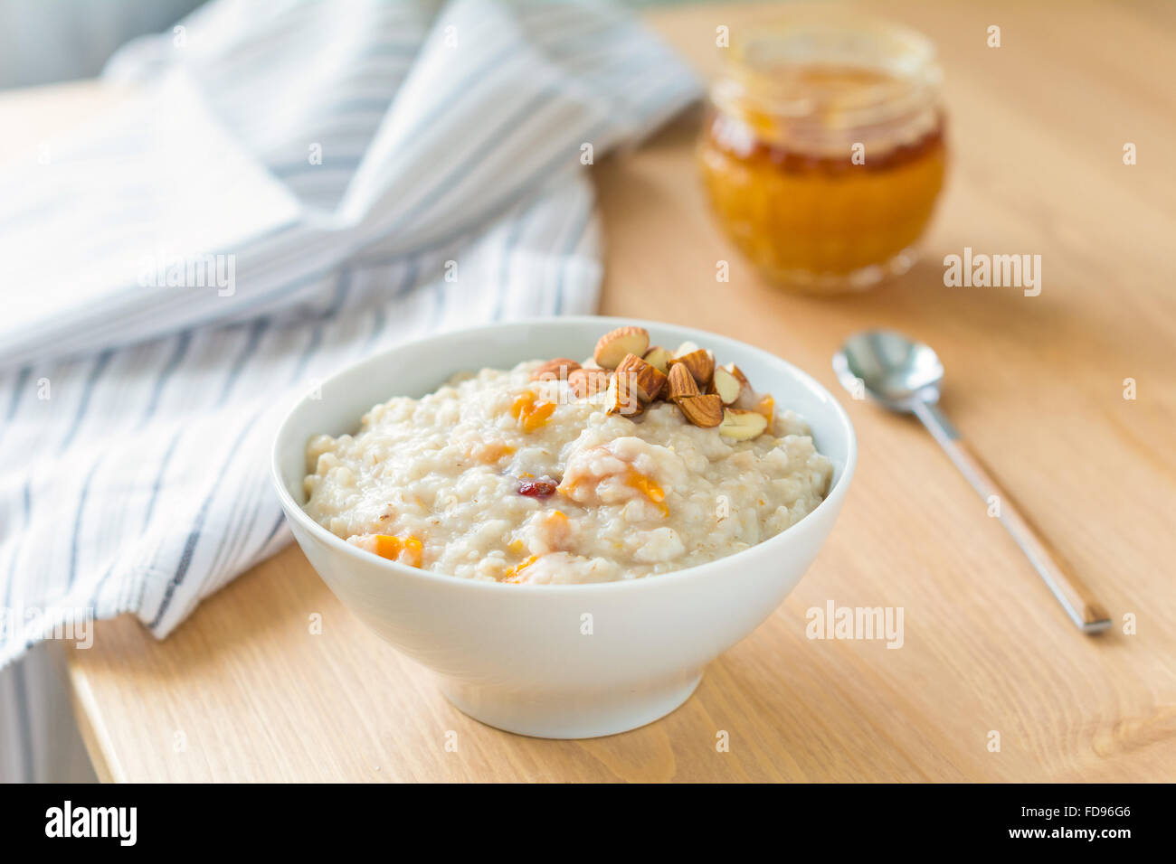 Gruau d'avoine avec des abricots secs et amandes hachées sur table en bois clair. Pot de miel sur l'arrière-plan Banque D'Images