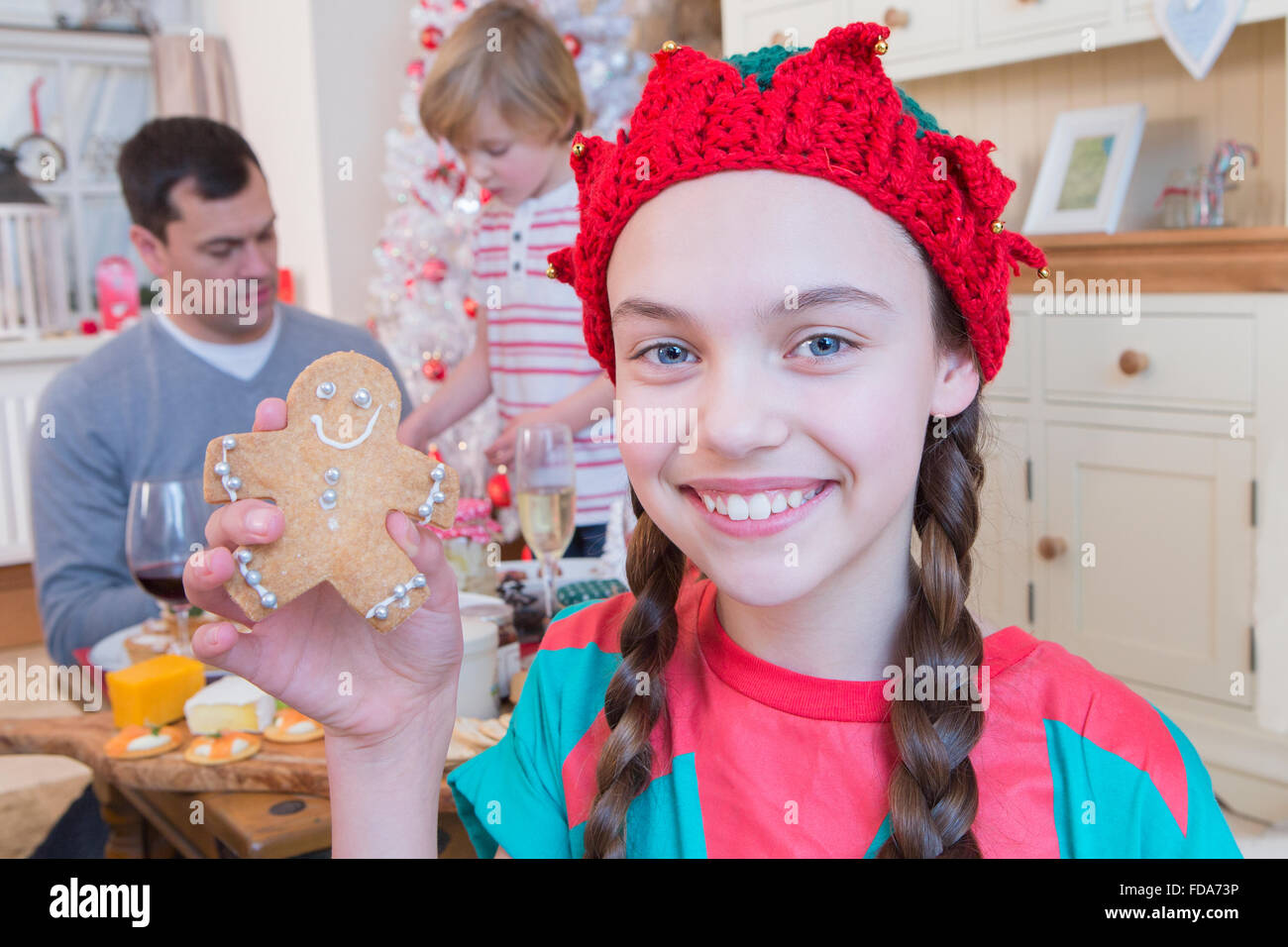 Jeune fille habillé comme un elfe à l'époque de Noël avec son père et son frère dans l'arrière-plan. Elle sourit à l'appareil photo et la tenue Banque D'Images